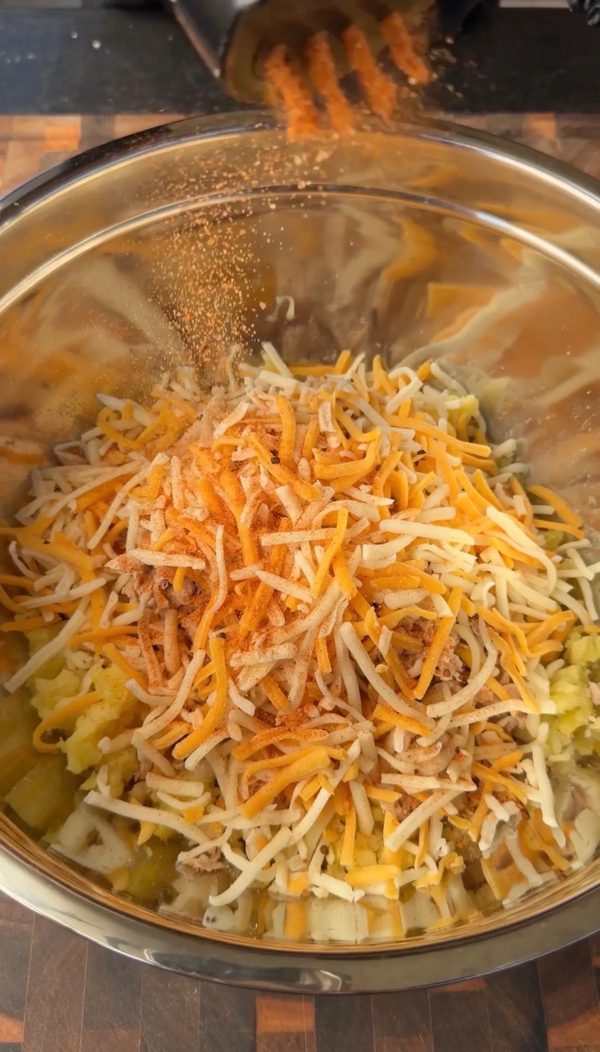 Shredded chicken and mashed potato mixture topped with shredded cheese and smoked paprika being added in a large mixing bowl
