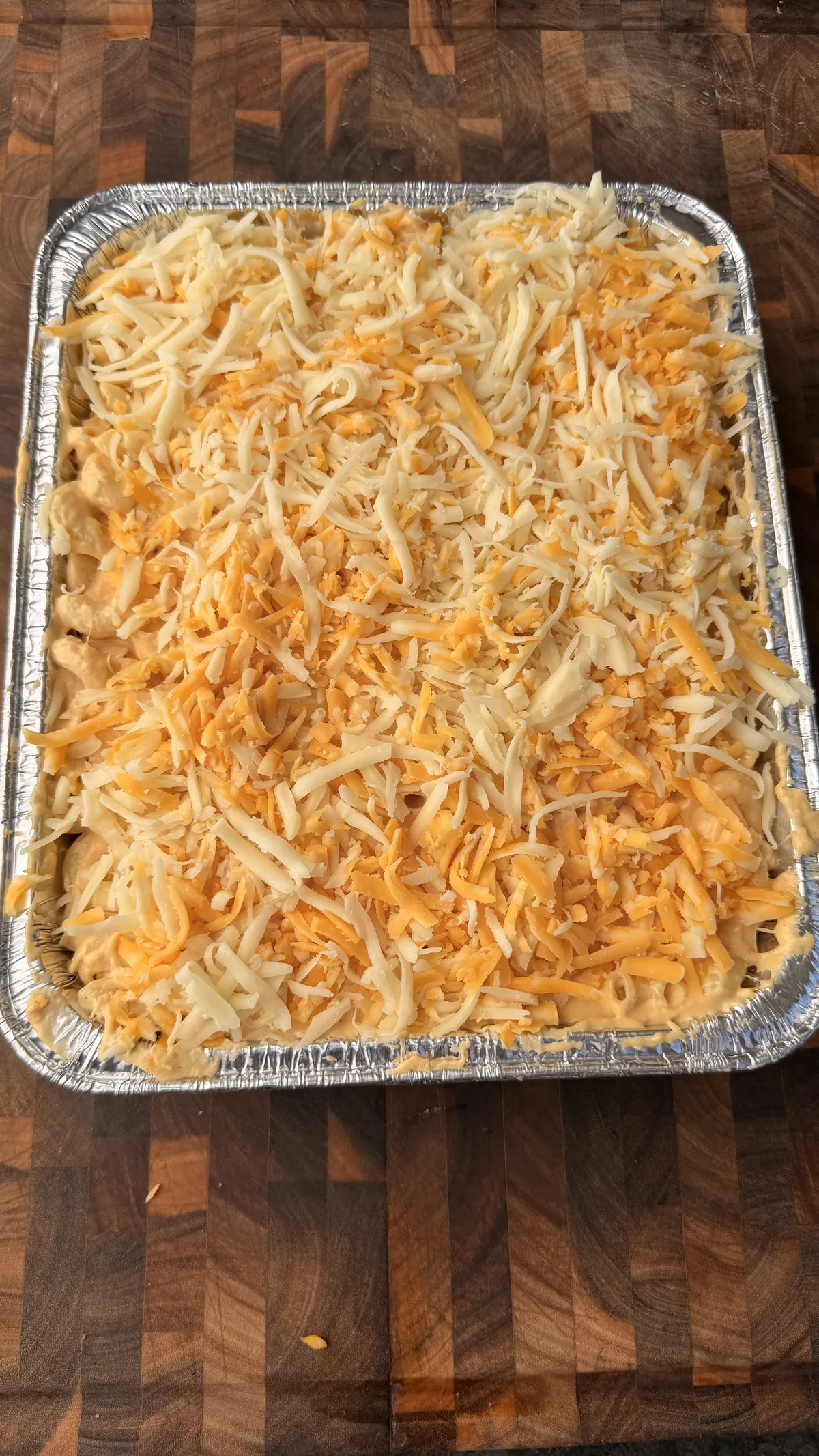 Aluminum pan of elbow macaroni topped with freshly shredded mozzarella, Colby Jack, and sharp cheddar cheese, unbaked
