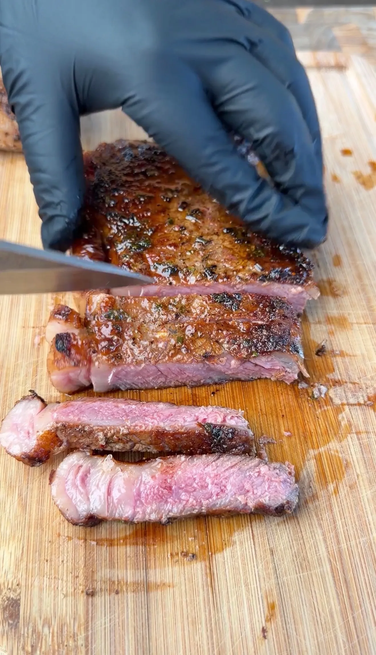 Gloved hands slicing a juicy, herb-crusted steak on a wooden cutting board with a pink medium-rare interior