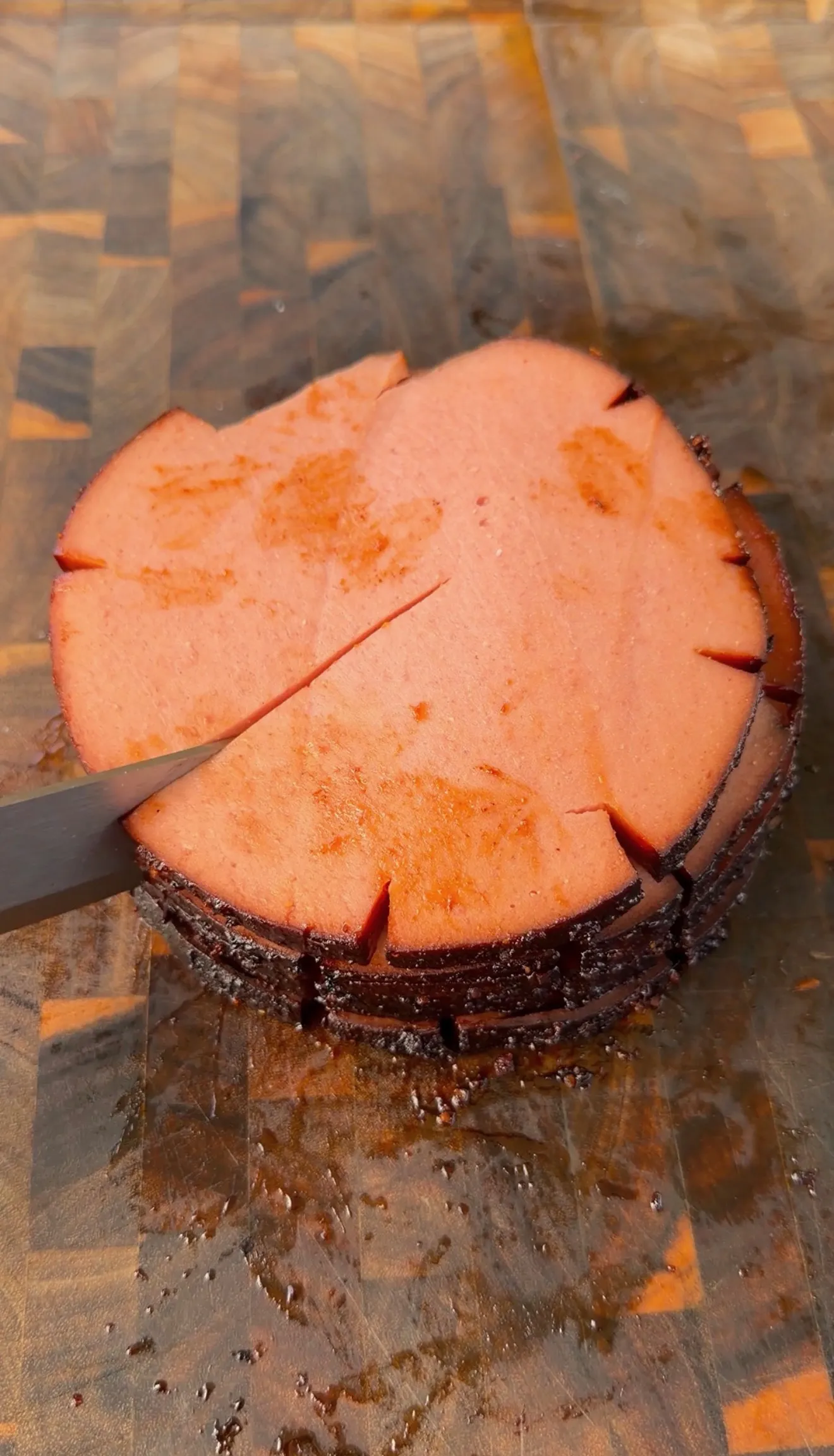 Thick smoked bologna chub with scored top being sliced on a wooden end-grain cutting board