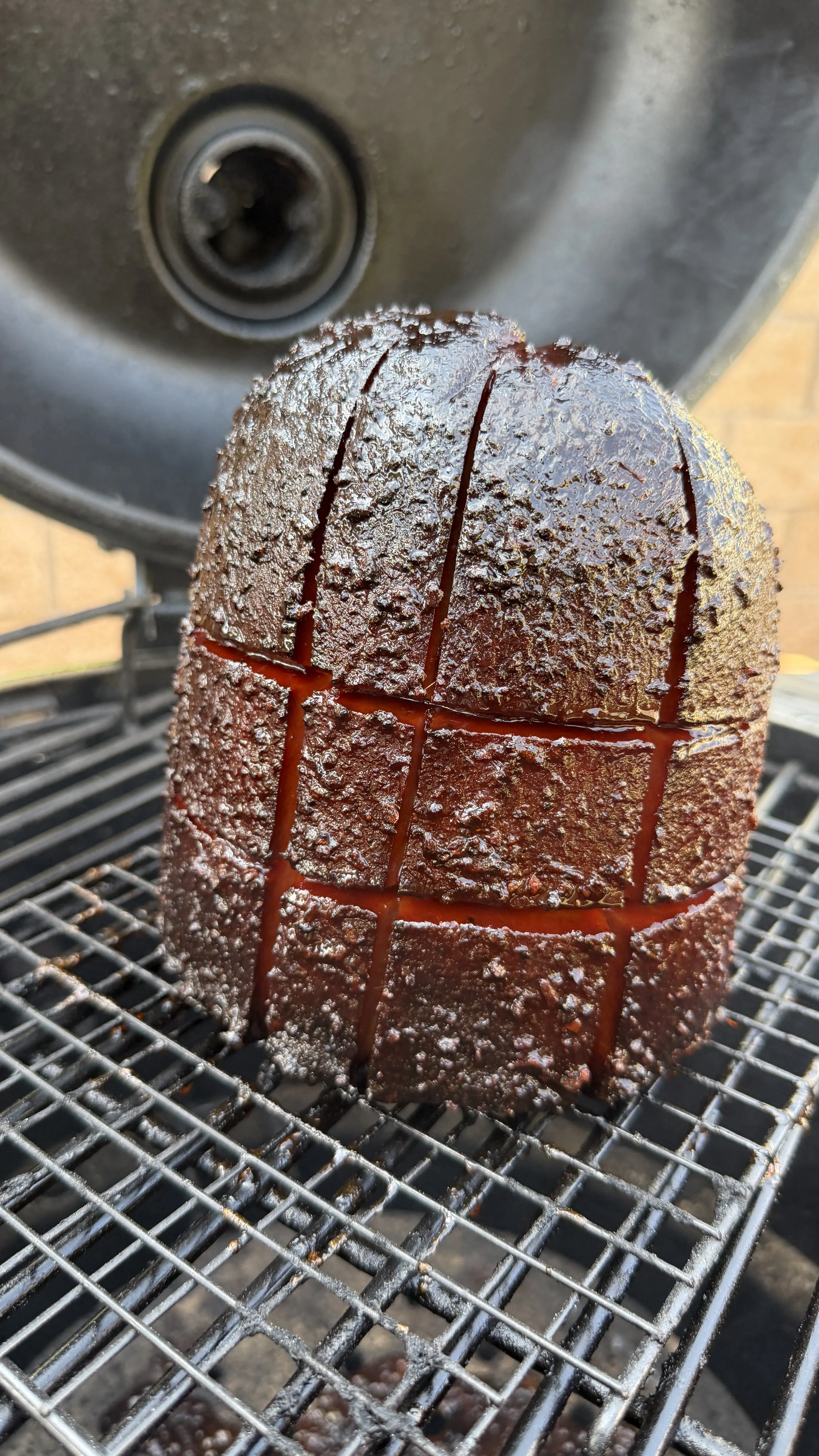 Whole bologna chub with crosshatch score marks and dark bark resting on smoker grill grates
