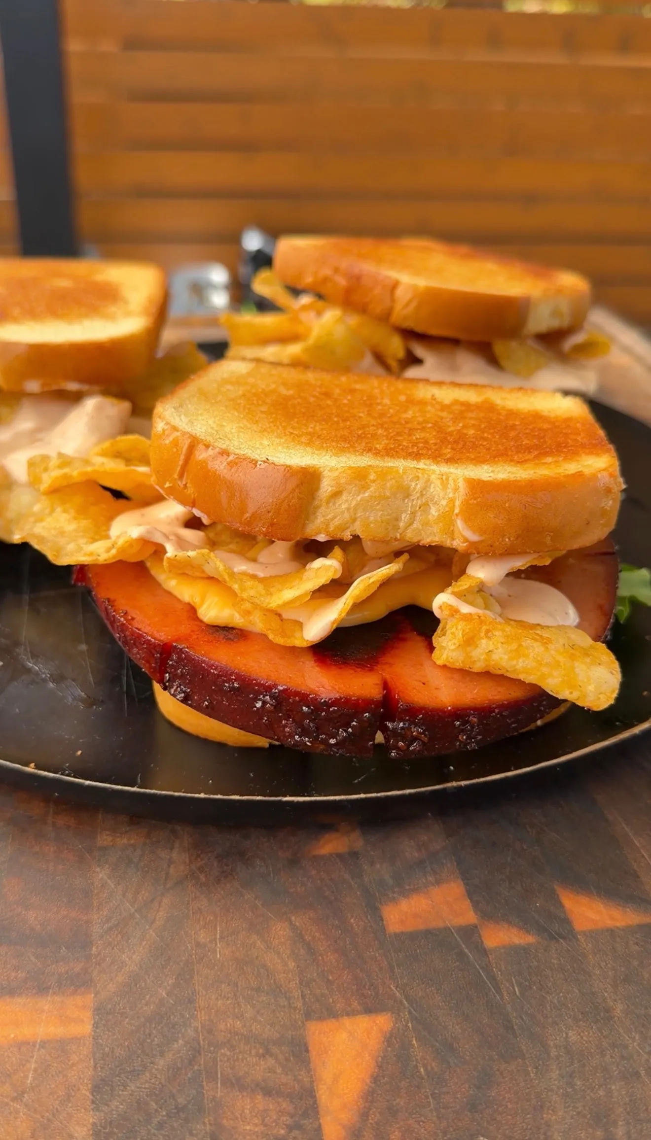 Smoked and fried bologna sandwich with potato chips and sauce on toasted bread, served on a dark plate