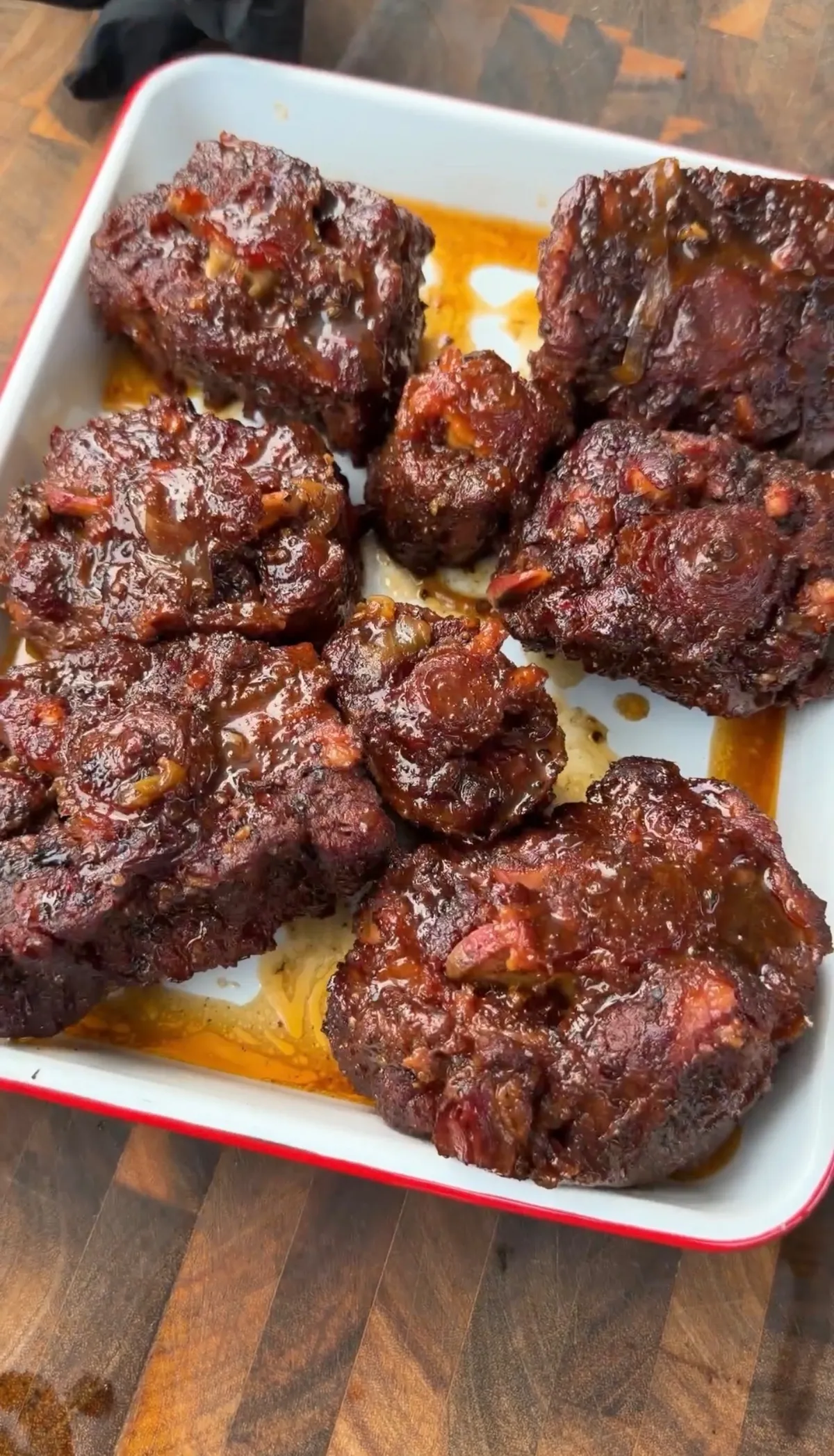 Fork-tender smoked oxtails with glossy brown sugar bourbon braise in a white baking dish on a wood surface