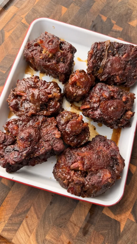 Fork-tender smoked oxtails with glossy brown sugar bourbon braise in a white baking dish on a wood cutting board