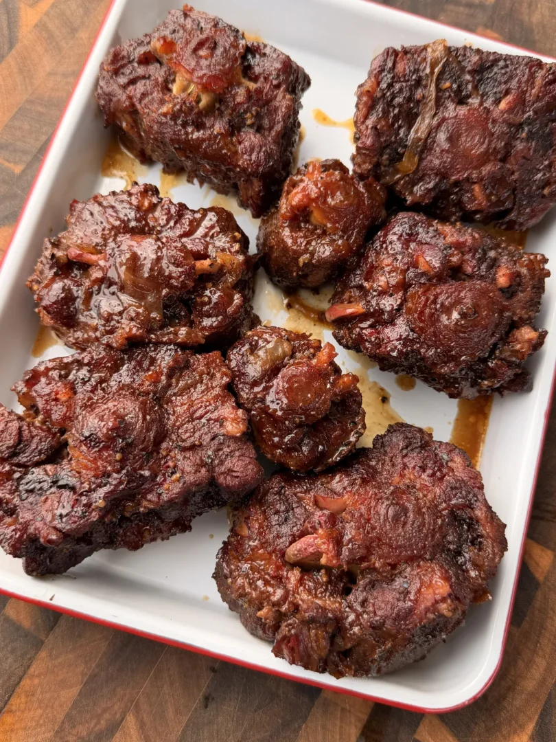 Fork-tender smoked oxtails with glossy brown sugar bourbon braise in a white baking dish on a wood cutting board