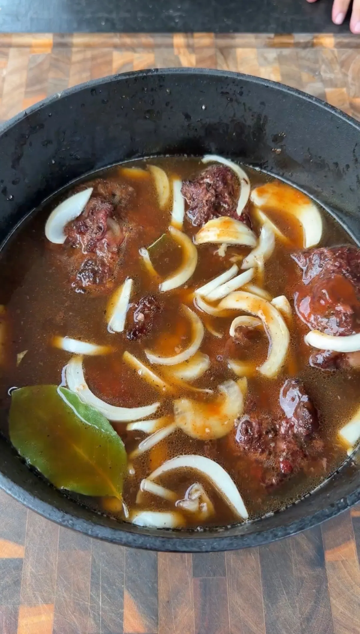 Smoked oxtails in a Dutch oven with bourbon braising liquid, sliced yellow onion, and bay leaves