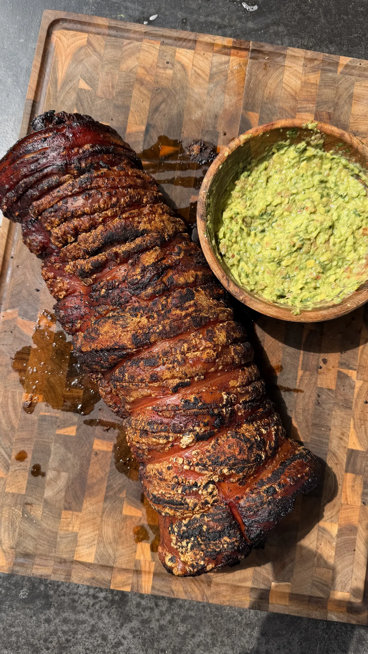 Smoky spice-rubbed pork belly porchetta roll on a wooden cutting board with a bowl of chunky guacamole