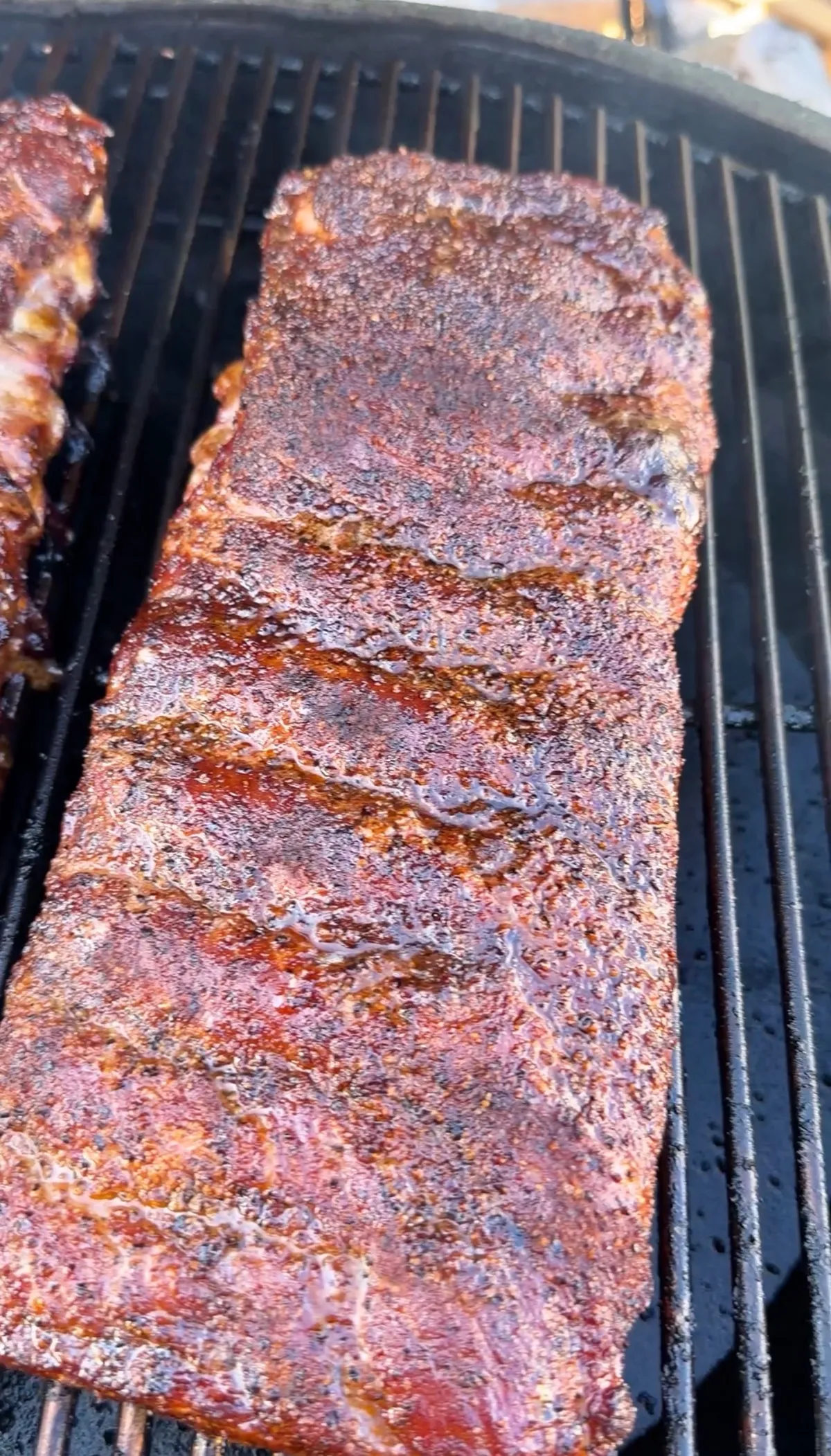 A rack of smoked ribs with a deep mahogany bark and glistening glaze resting on black grill grates