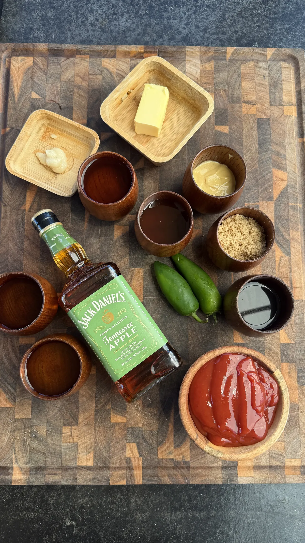 Smoked ribs BBQ sauce ingredients including Jack Daniel's Tennessee Apple, ketchup, jalapeños, butter, mustard, and brown sugar on a wooden cutting board