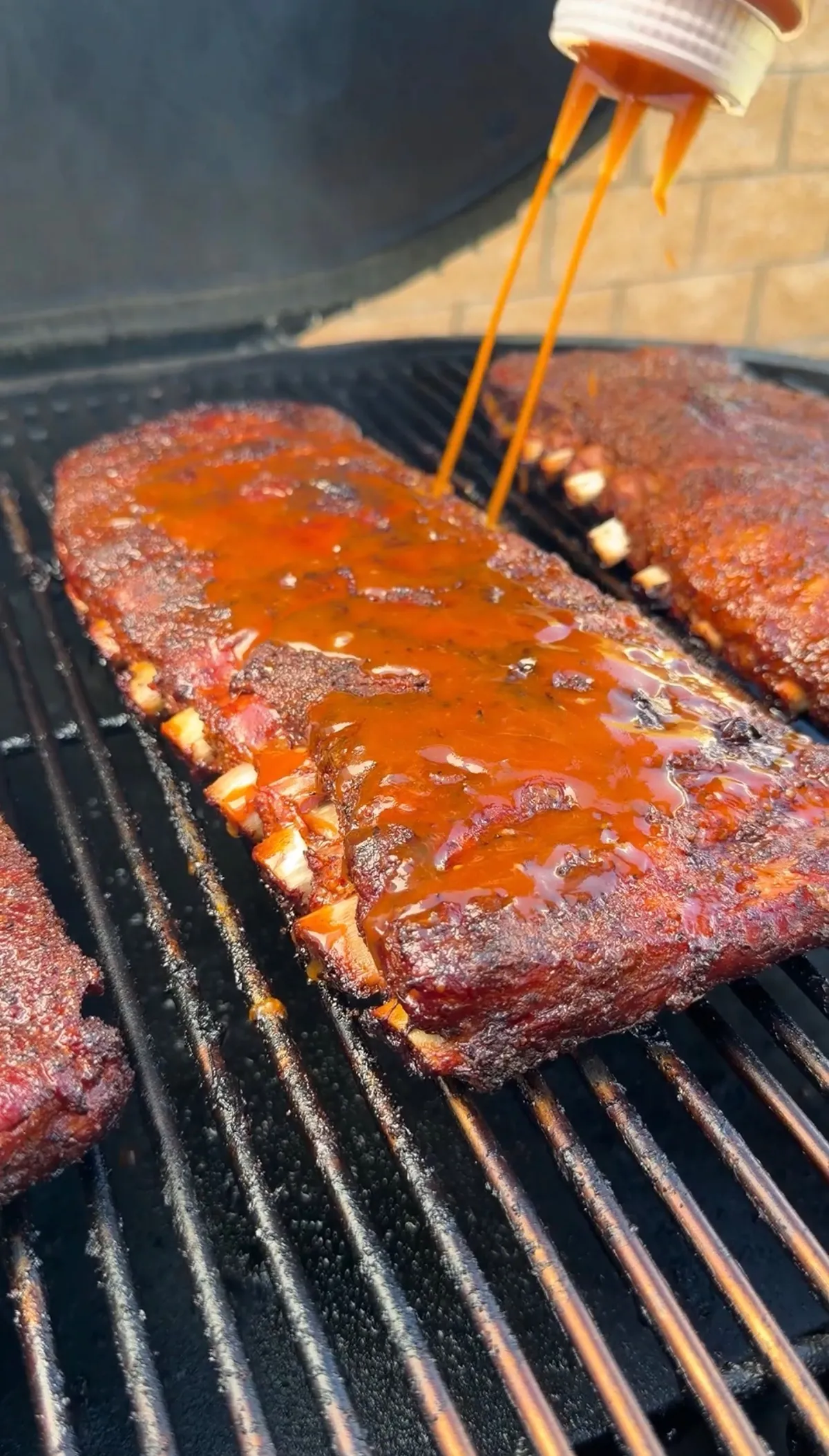 BBQ sauce being drizzled over smoky pork ribs on a charcoal grill grate