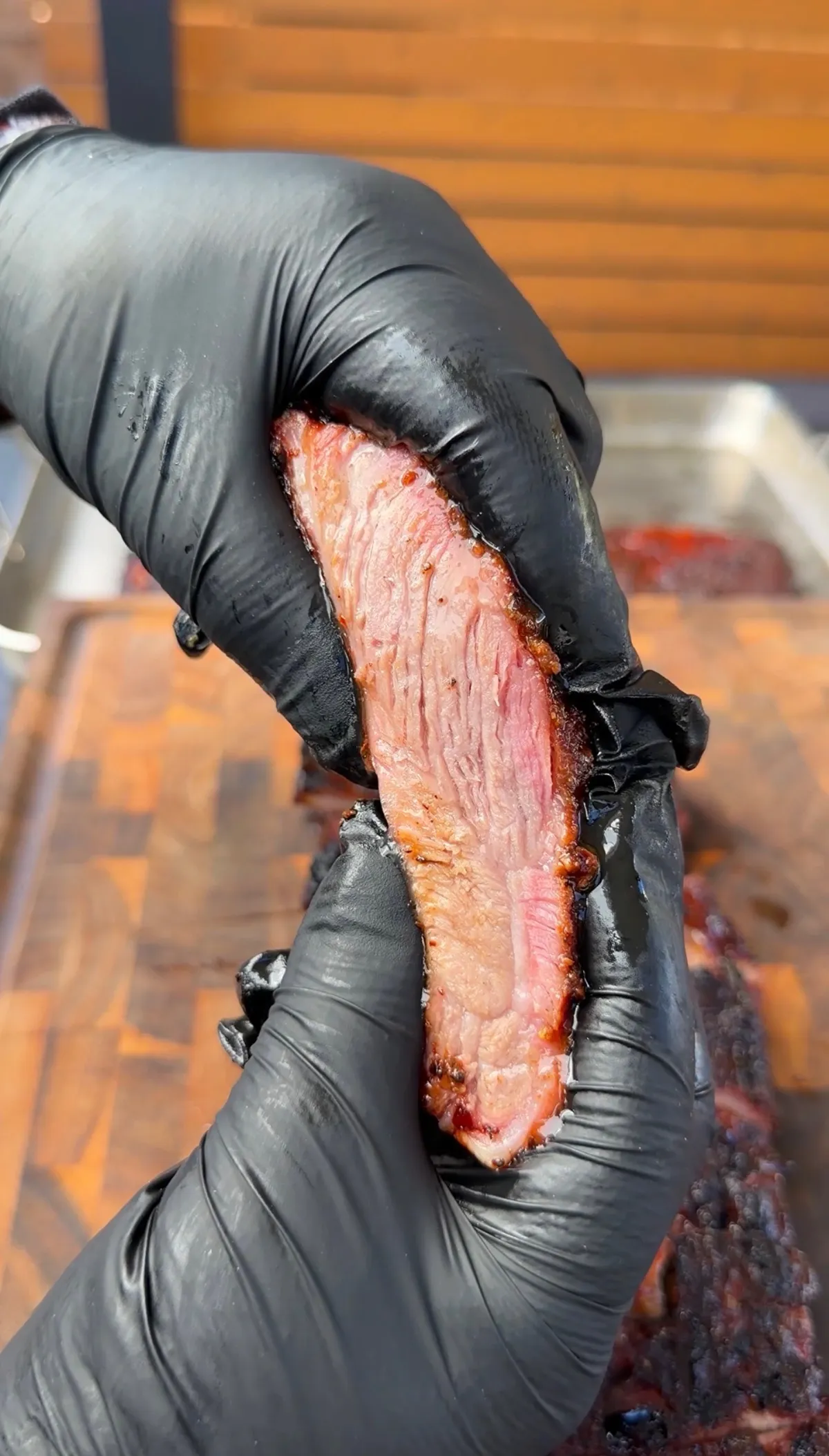 Gloved hands performing a bend test on a juicy smoked St. Louis spare rib with pink smoke ring and dark bark