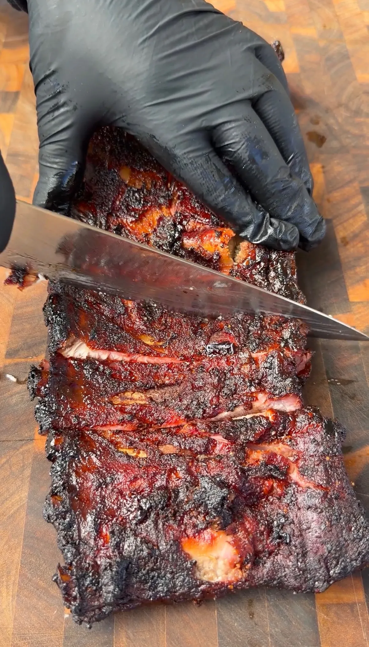 Apple cider smoked St. Louis spare ribs being sliced on a wooden cutting board with black gloved hands