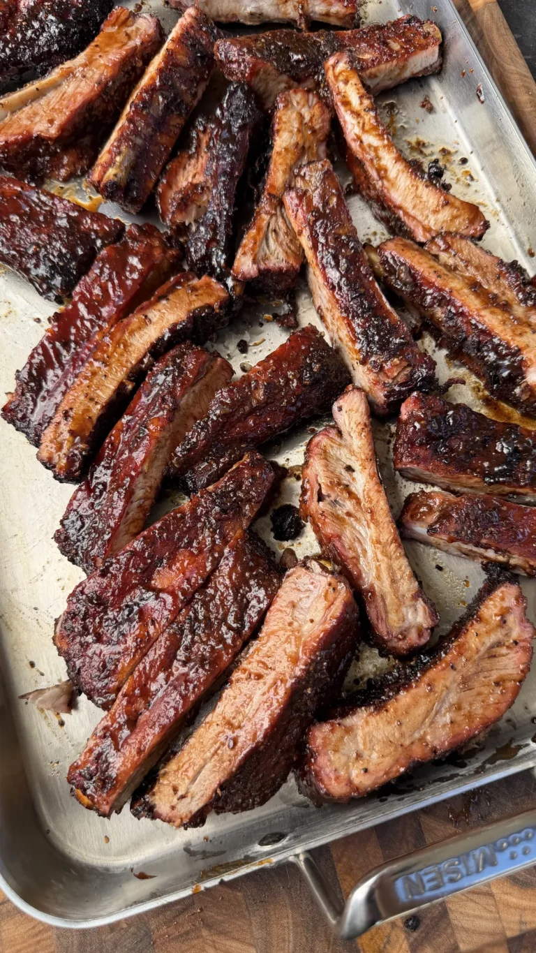 Apple cider glazed smoked St. Louis spare ribs, sliced and piled on a stainless steel sheet pan