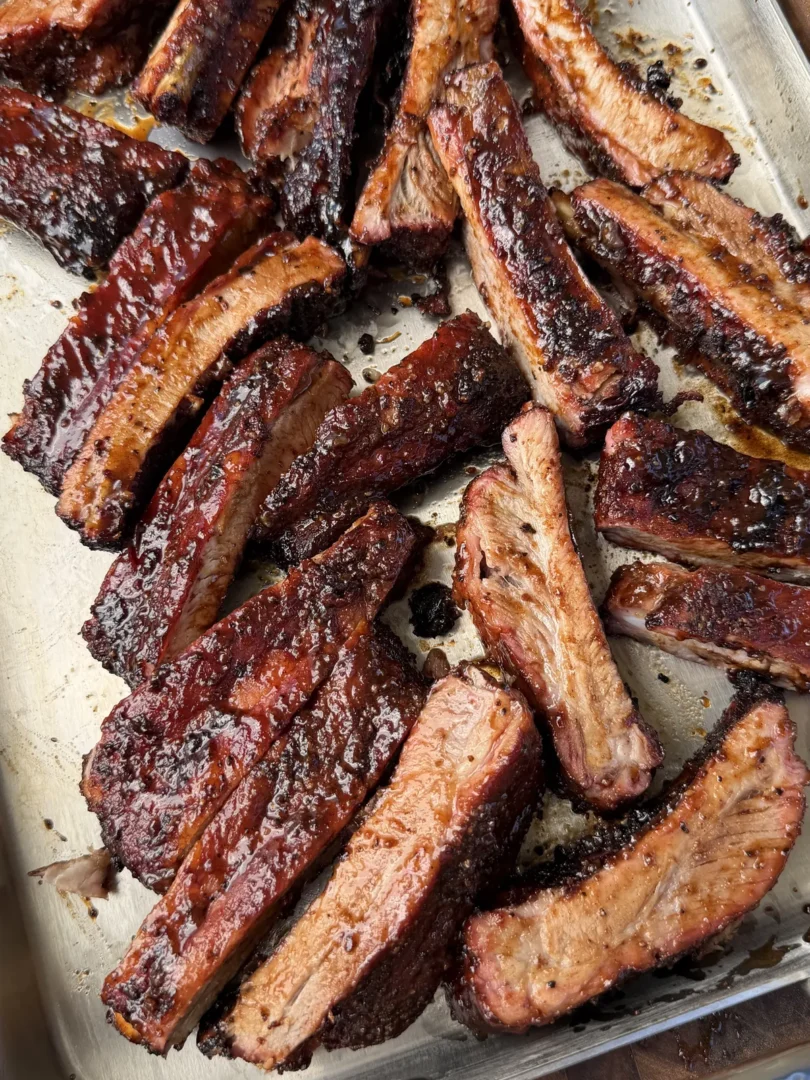 Apple cider glazed smoked St. Louis spare ribs, sliced and piled on a stainless steel sheet pan