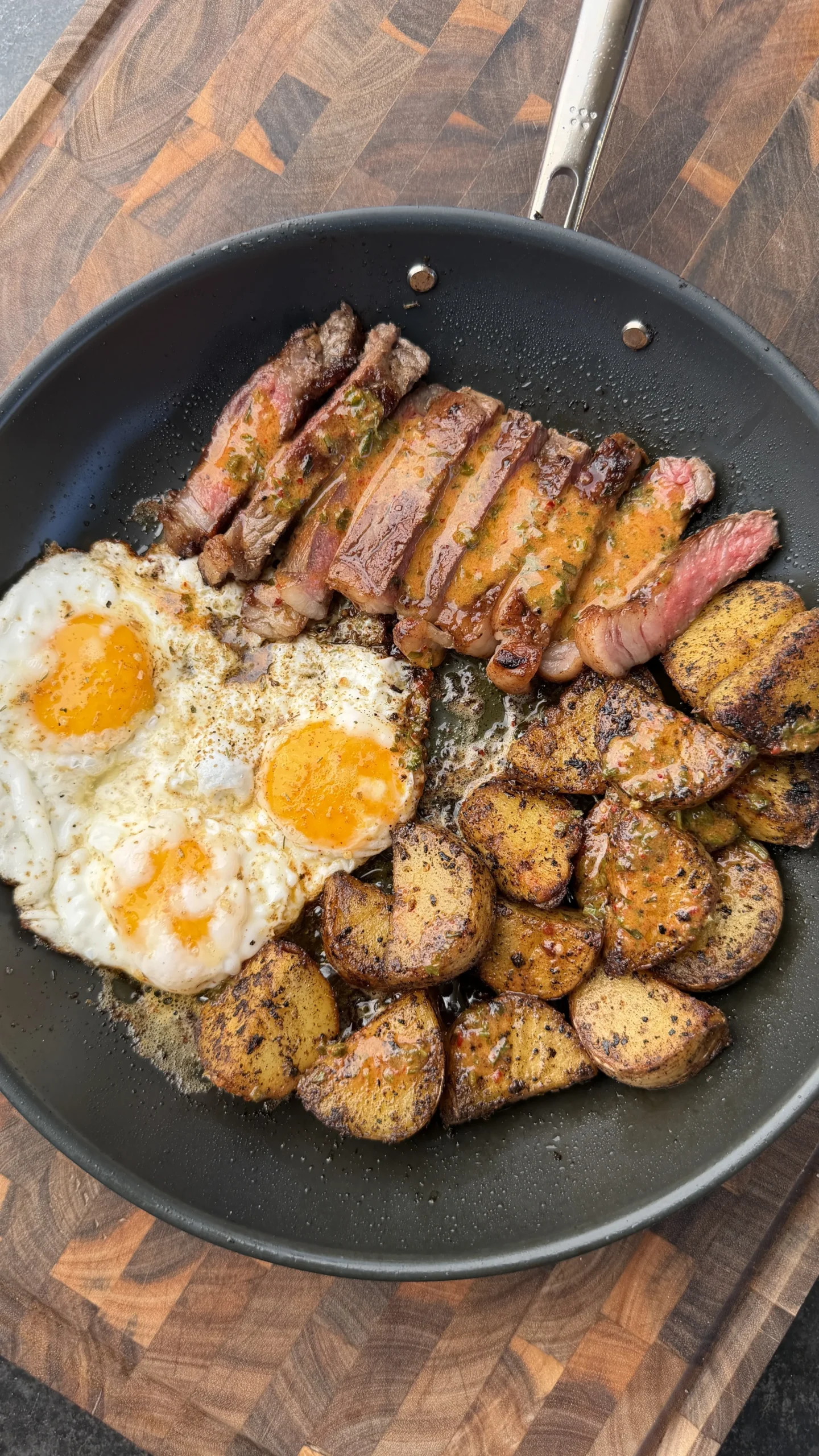 Sliced steak, fried eggs, and crispy potatoes with cowboy butter sauce in a black skillet