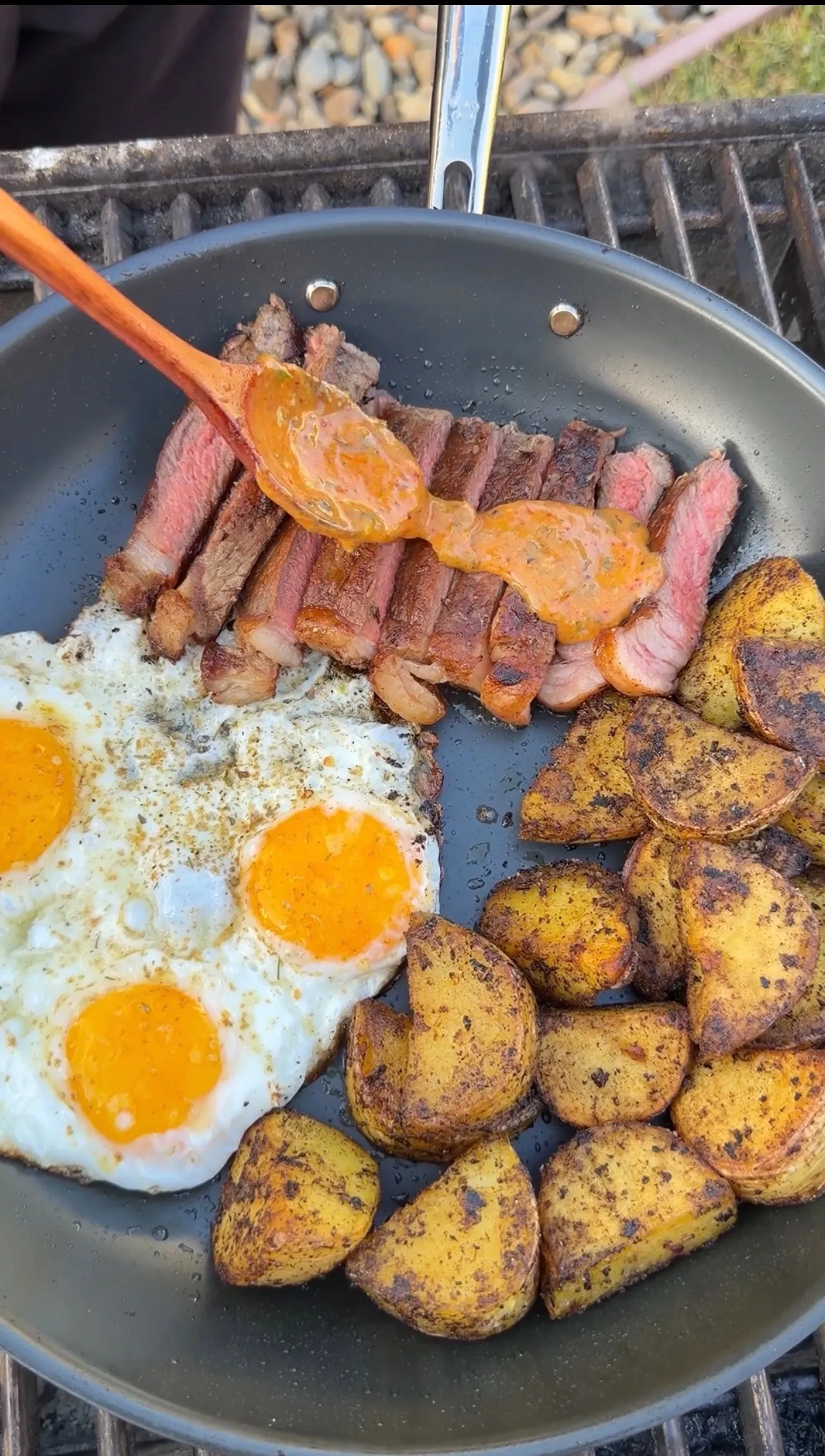 Sliced medium-rare steak, sunny-side-up eggs, and crispy potatoes in a skillet drizzled with cowboy butter