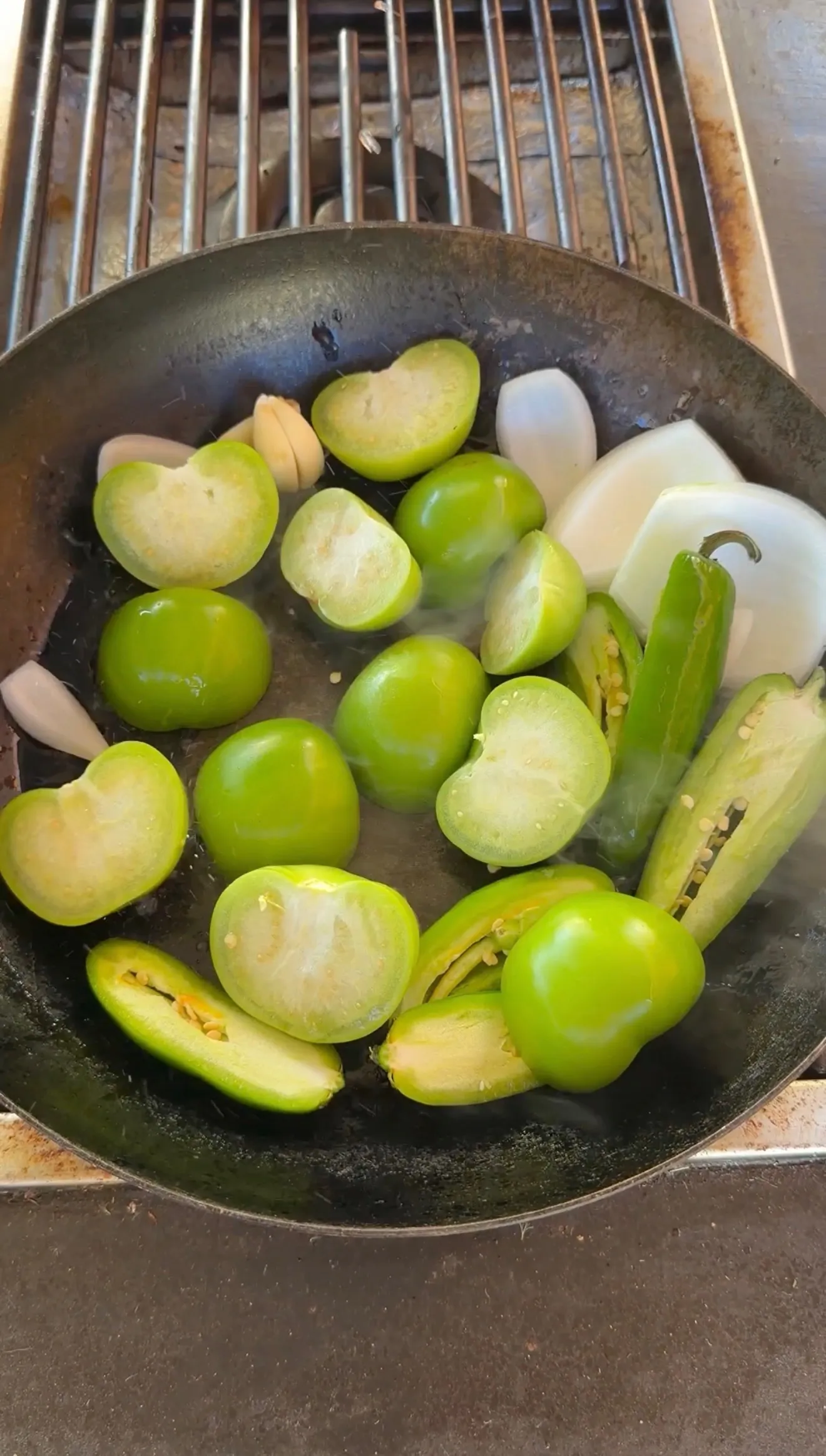 Fresh tomatillos, jalapeños, onion, and garlic roasting in a cast iron pan for salsa verde