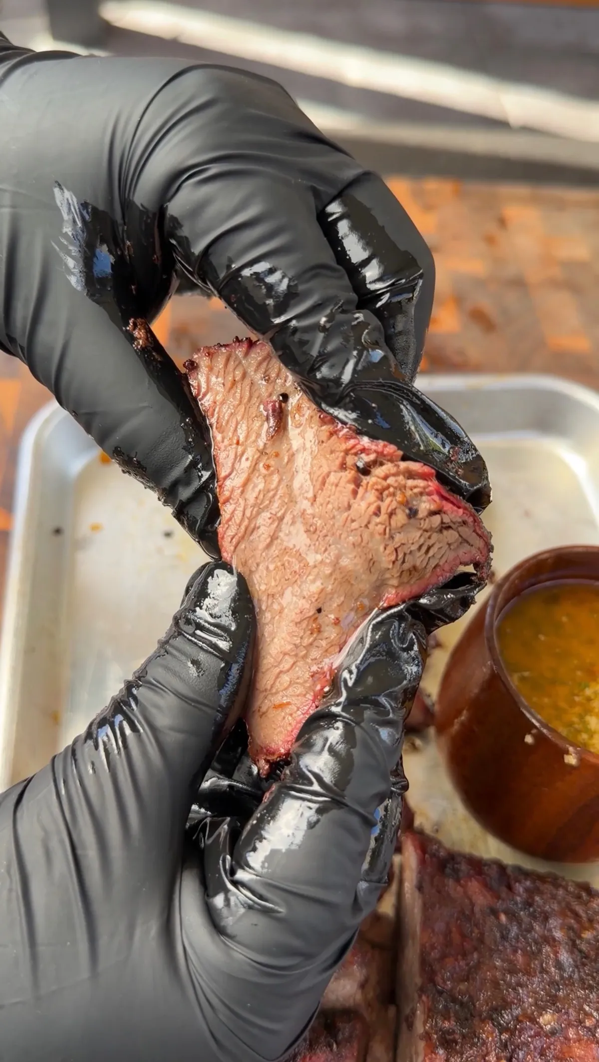 Gloved hands pulling apart juicy smoked trisket (tri-tip cooked like brisket) showing pink smoke ring and tender texture