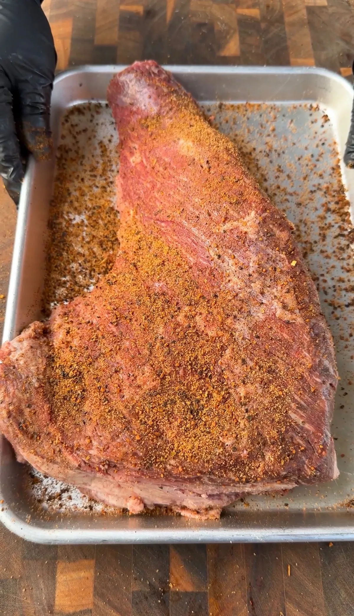 Raw tri-tip roast generously coated with orange-red dry rub seasoning in a metal baking pan