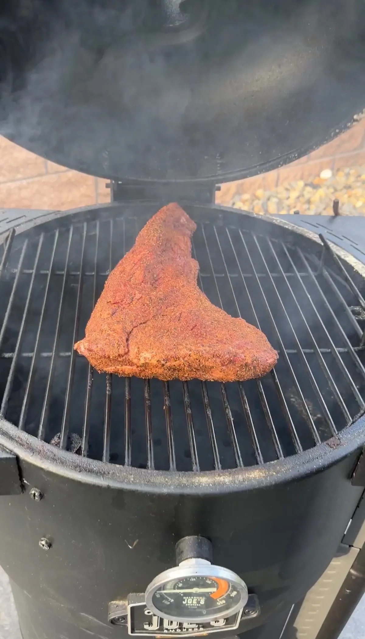 Heavily spice-rubbed tri-tip brisket-style on a Kamado Joe smoker grill with smoke rising