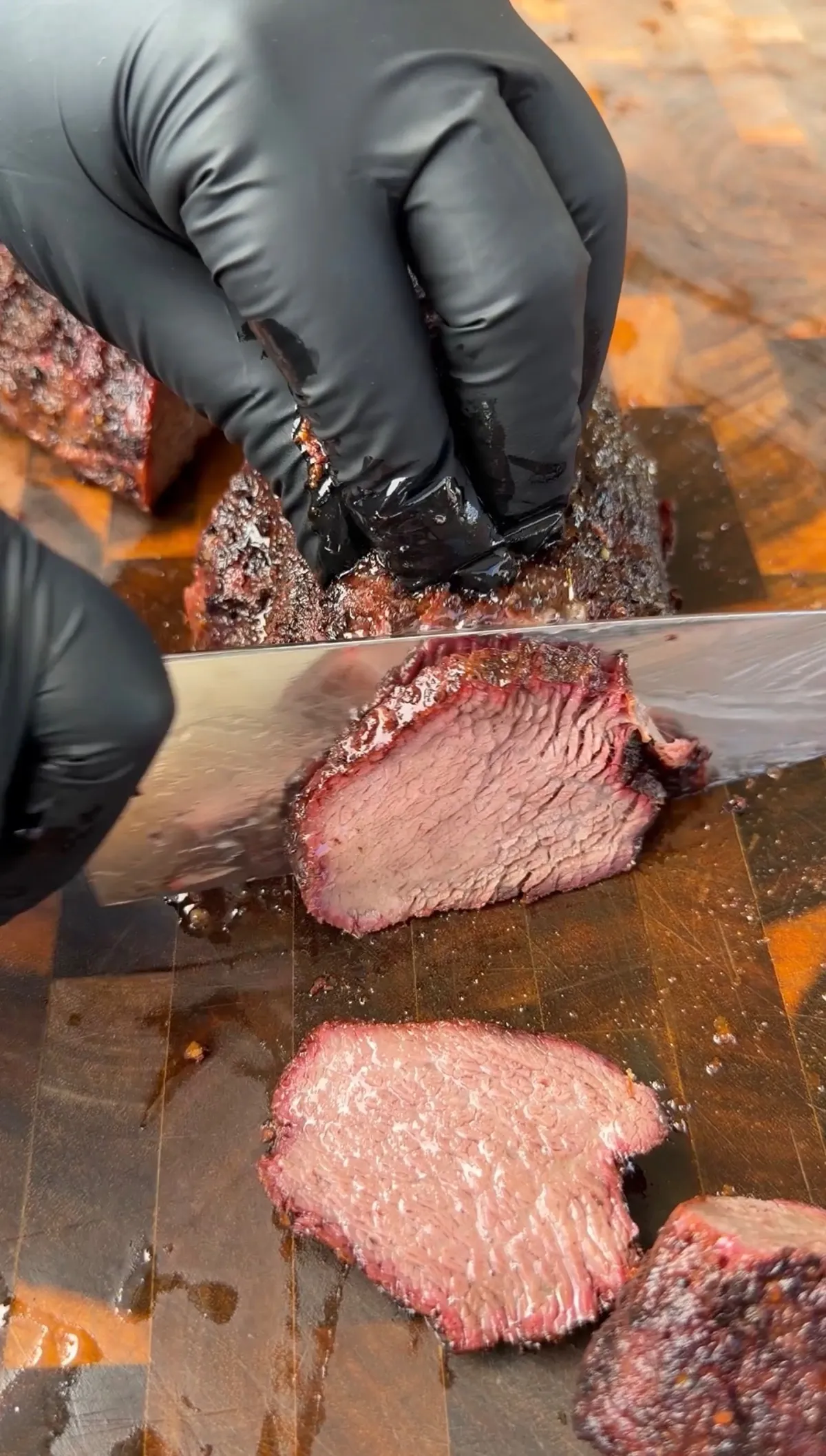 Gloved hands slicing smoked trisket (tri-tip cooked like brisket) showing pink smoke ring on wooden cutting board