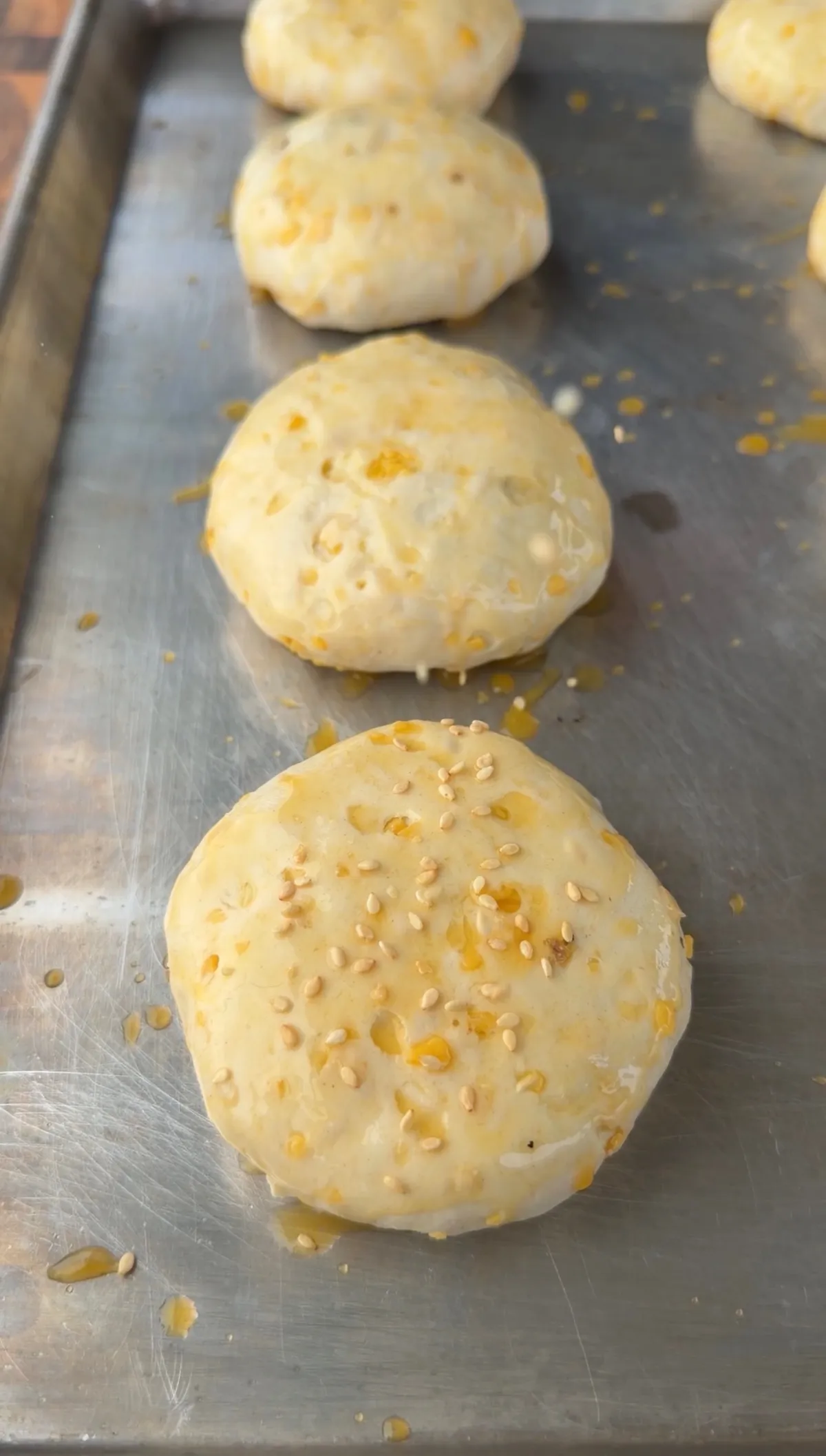 Raw cheeseburger bombs made with biscuit dough, topped with egg wash and sesame seeds on a metal baking sheet