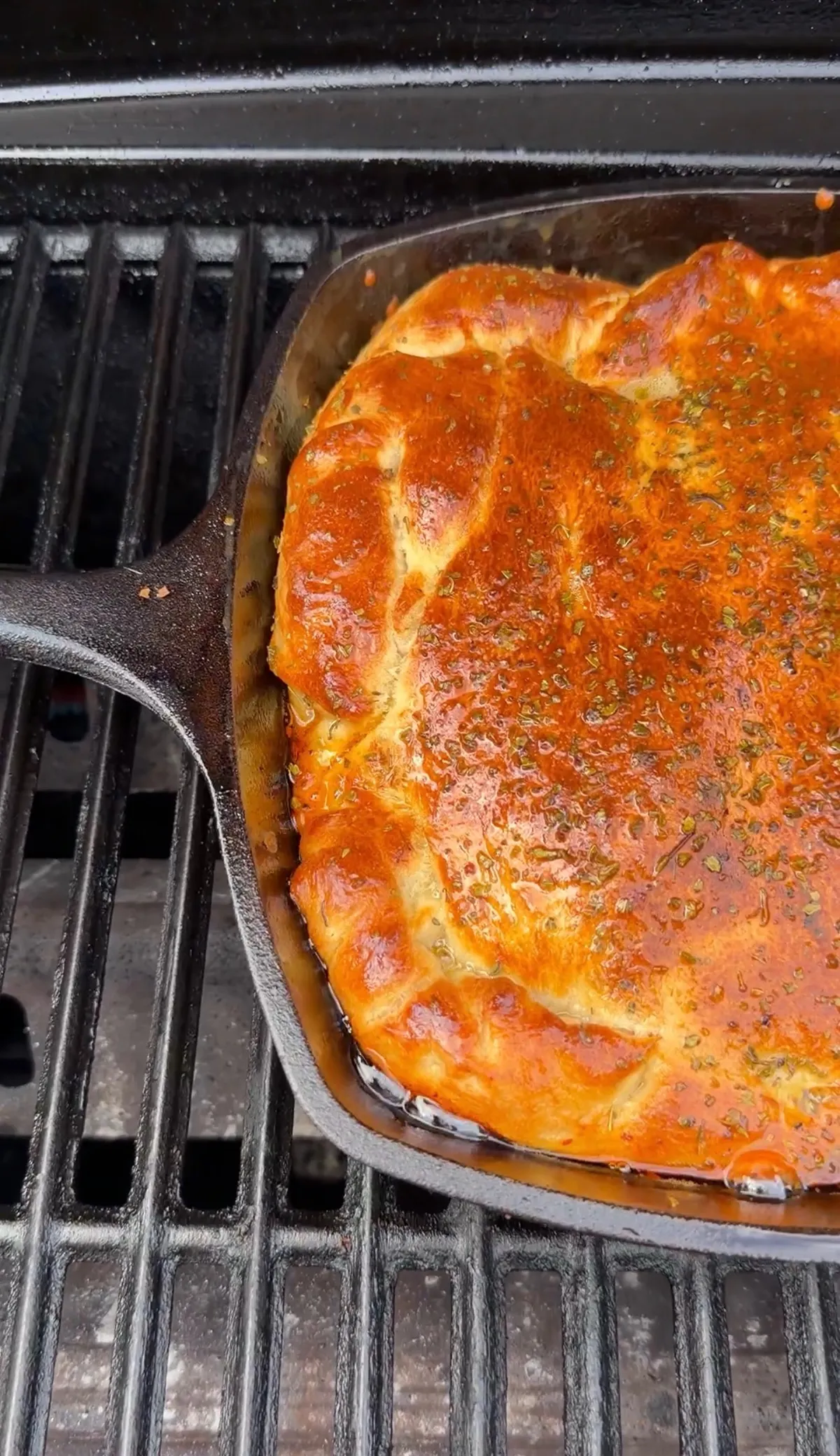 Pillsbury pizza dough brushed with egg wash and oregano baking golden brown in a square cast-iron skillet on a grill