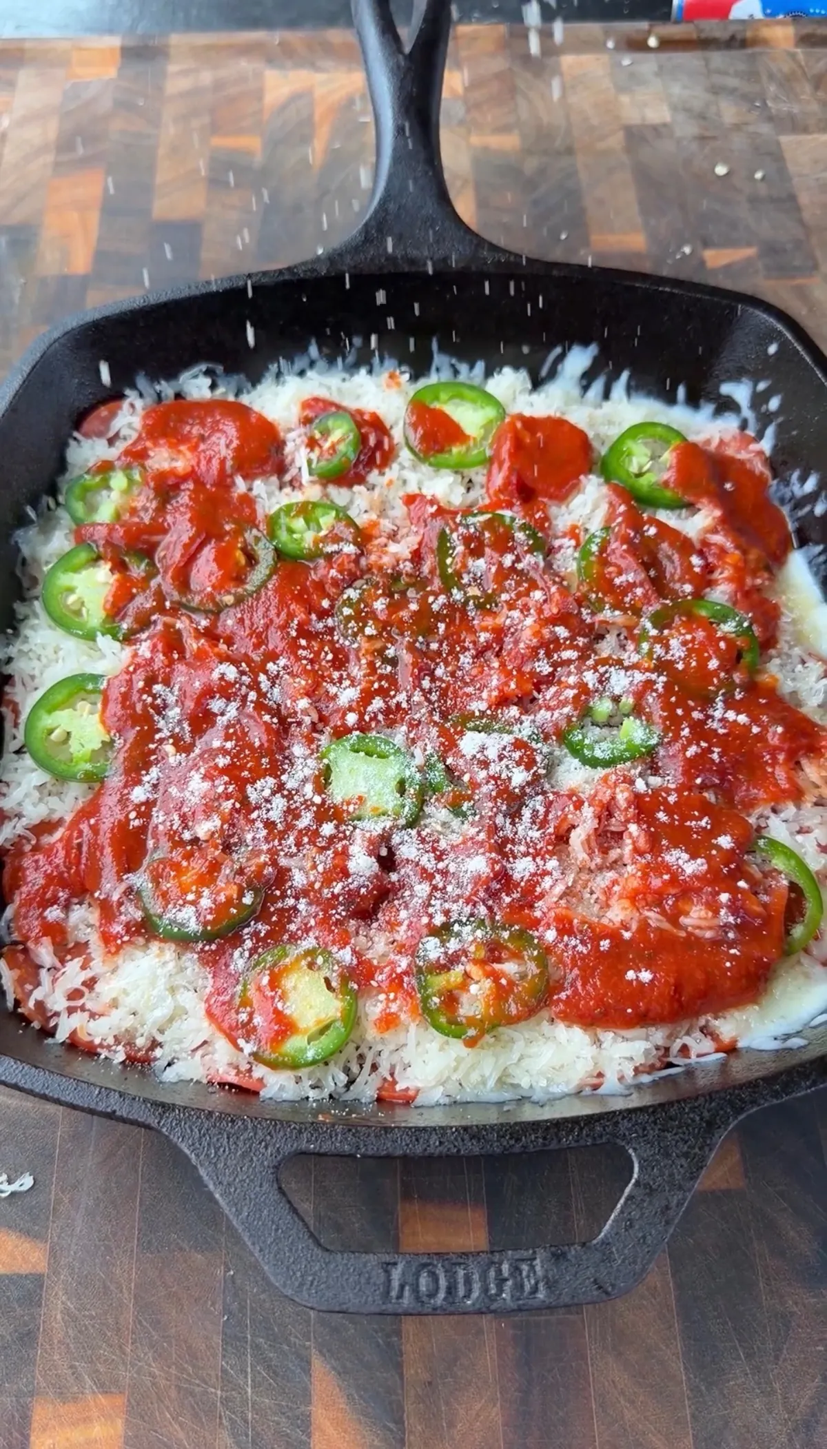 Unbaked upside-down deep dish pizza with marinara, mozzarella, pepperoni, jalapeño rounds, and Parmesan in a Lodge cast-iron skillet