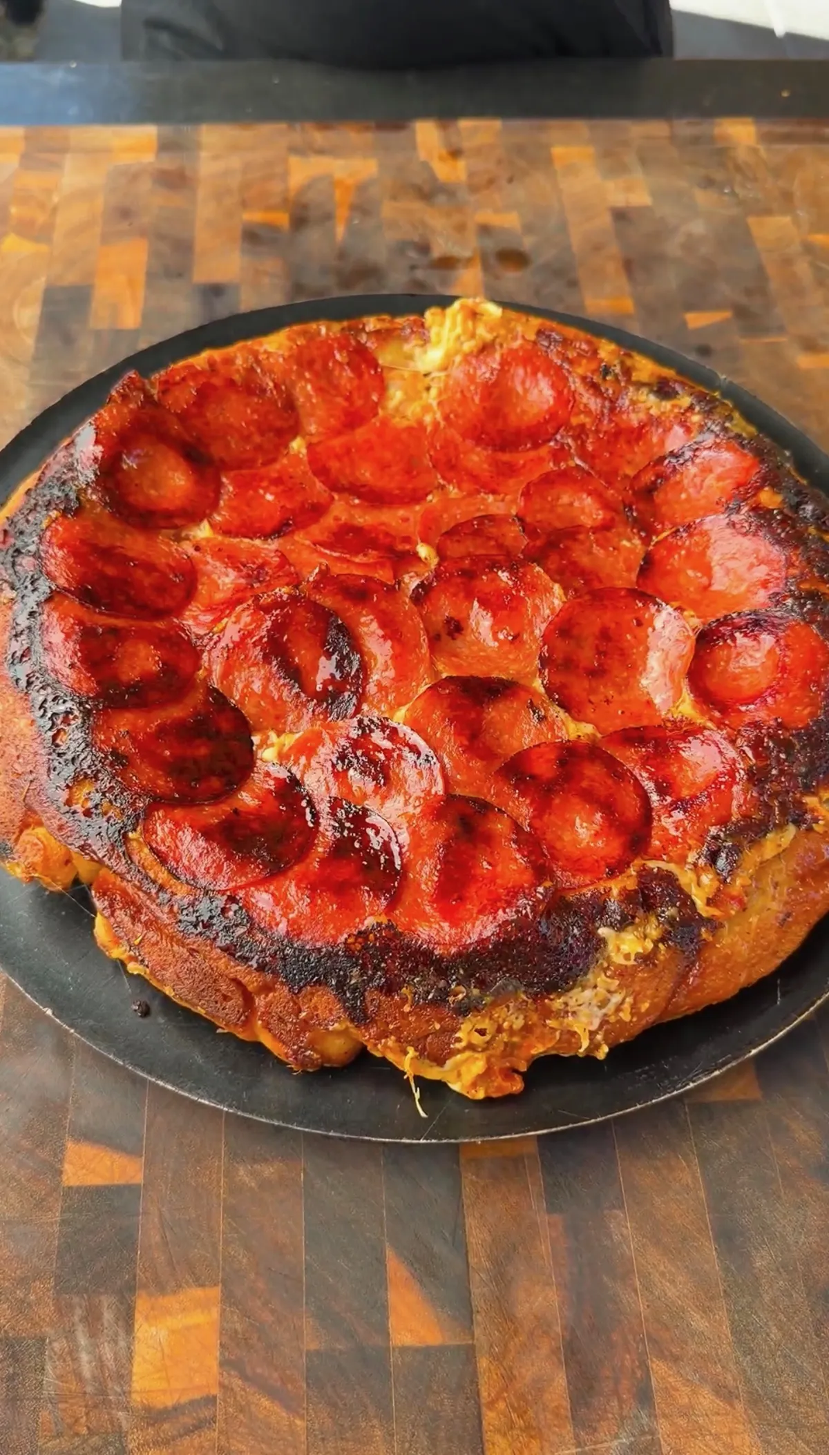 Upside down pepperoni pizza with crispy caramelized edges and charred pepperoni on a dark round pan