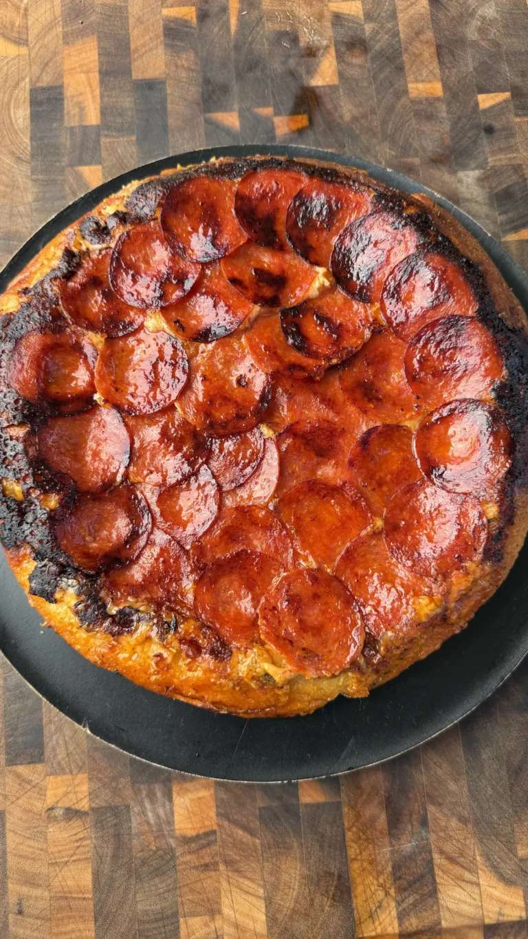 Upside down pepperoni pizza with caramelized crispy pepperoni on top, served on a black round pan over a wood board