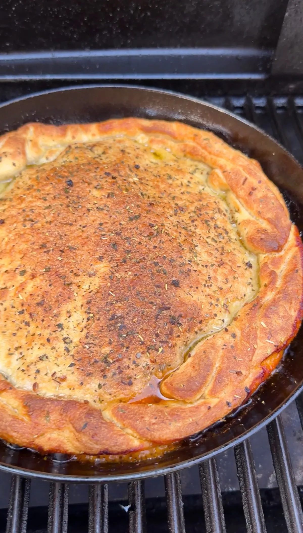 Golden-brown upside down pizza with herbs baked in a cast iron skillet on an outdoor grill