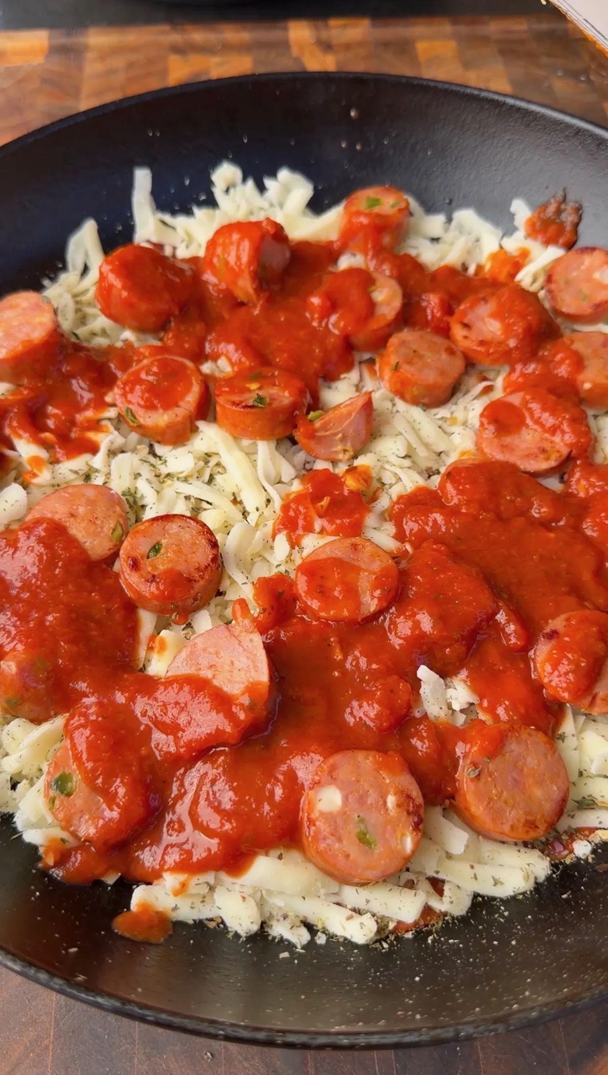 Skillet upside down pizza with sliced sausage and marinara sauce over shredded mozzarella cheese
