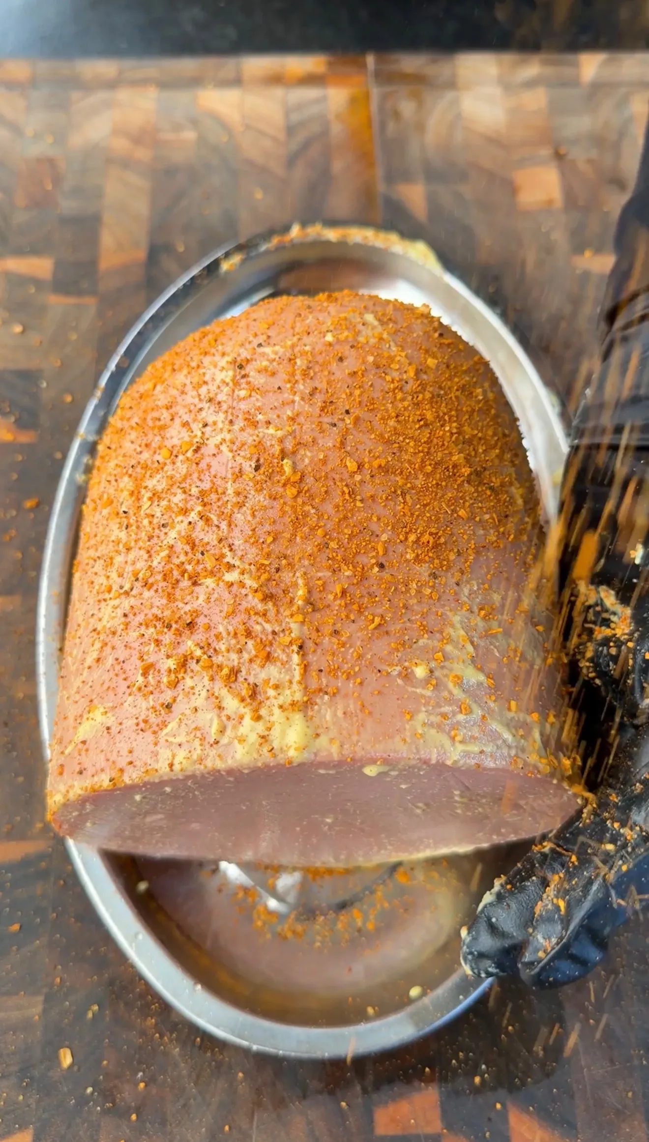 Whole bologna chub coated in orange spice dry rub sitting in a metal roasting pan on a cutting board