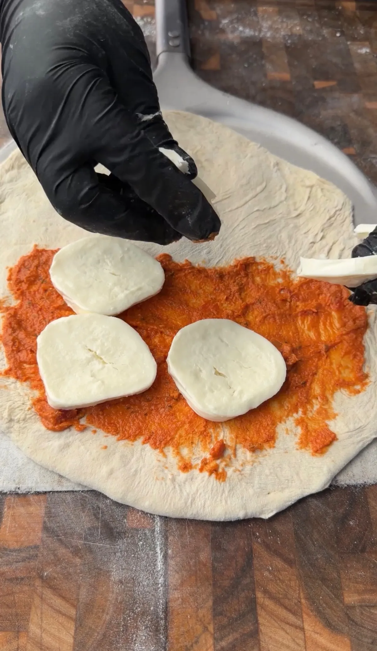Gloved hands placing fresh mozzarella slices onto pizza sauce spread over half of stretched calzone dough