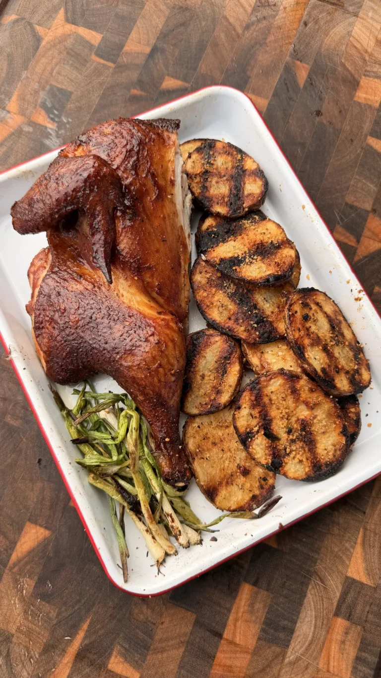 Applewood smoked BBQ spatchcock chicken with grilled Cajun Parmesan potatoes and charred green onions on a white tray