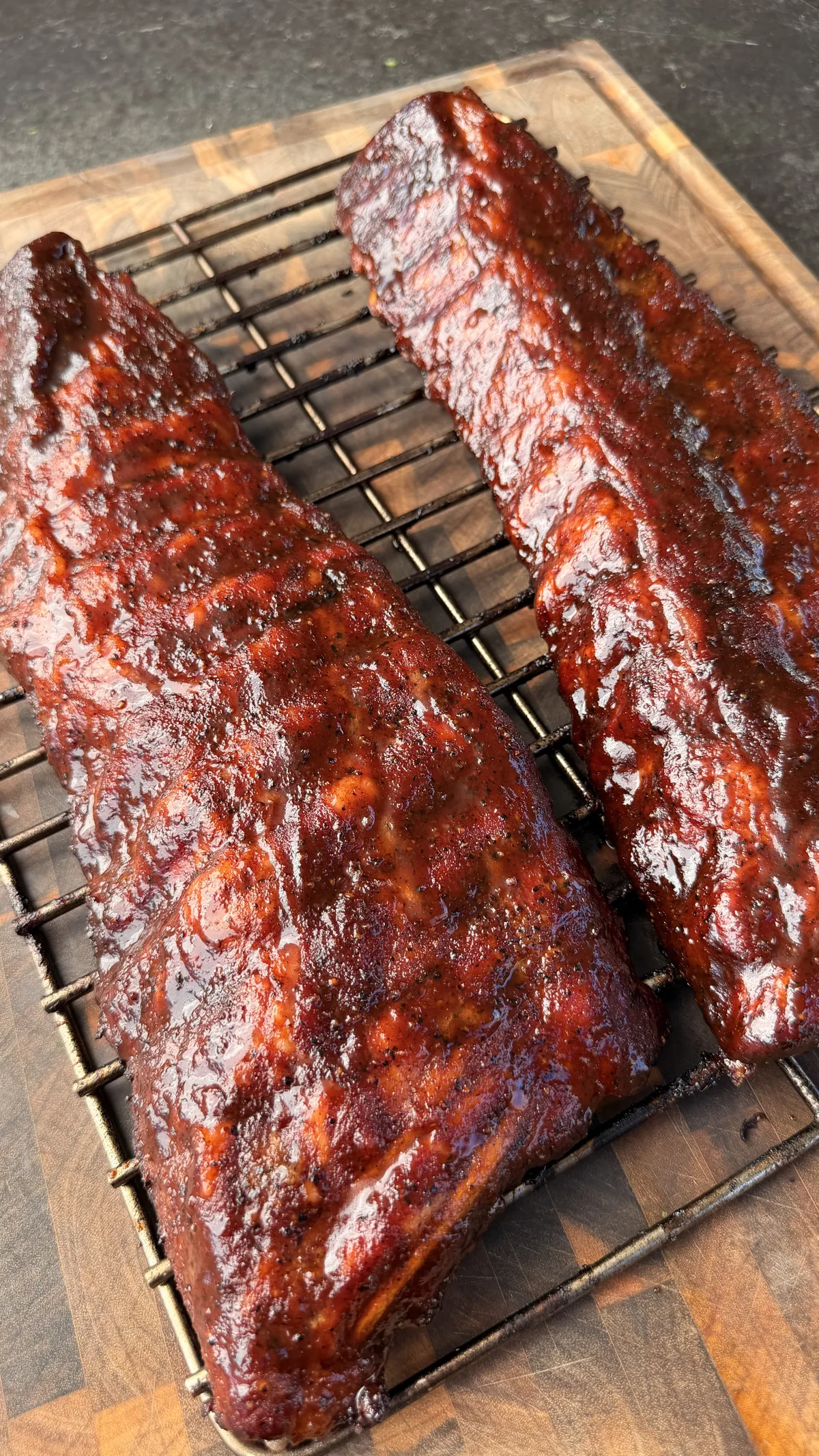 Two racks of applewood-smoked baby back ribs glazed with sticky honey BBQ sauce resting on a wire rack over a wooden cutting board
