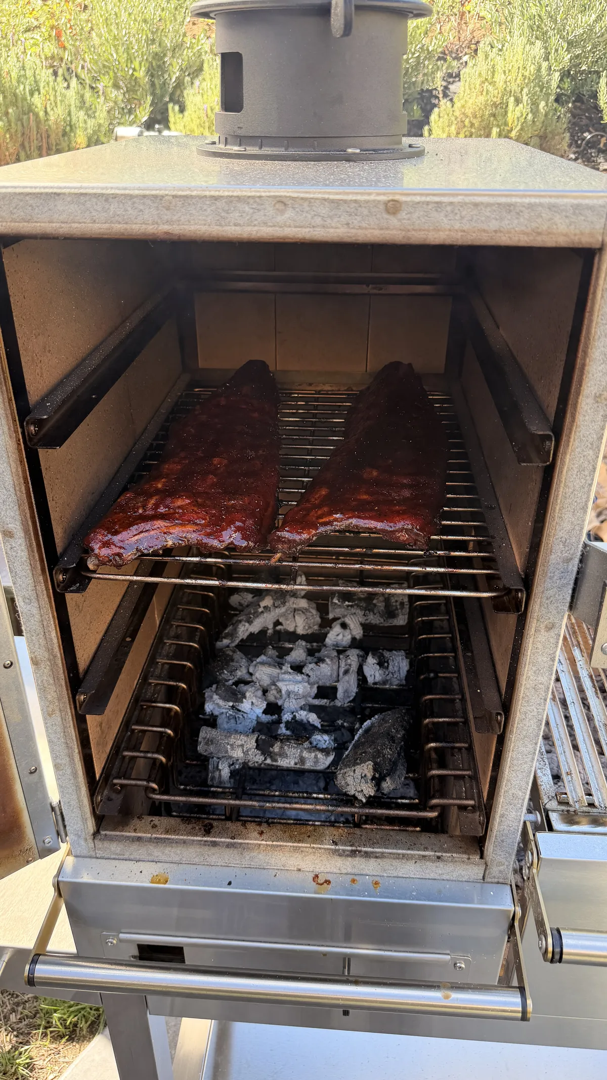 Two racks of chipotle BBQ rubbed baby back ribs smoking over charcoal in an applewood smoker