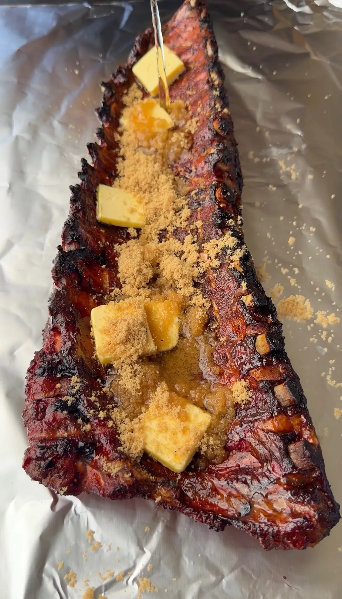 Baby back ribs on foil topped with butter pats and brown sugar before wrapping, ready to braise with apple juice