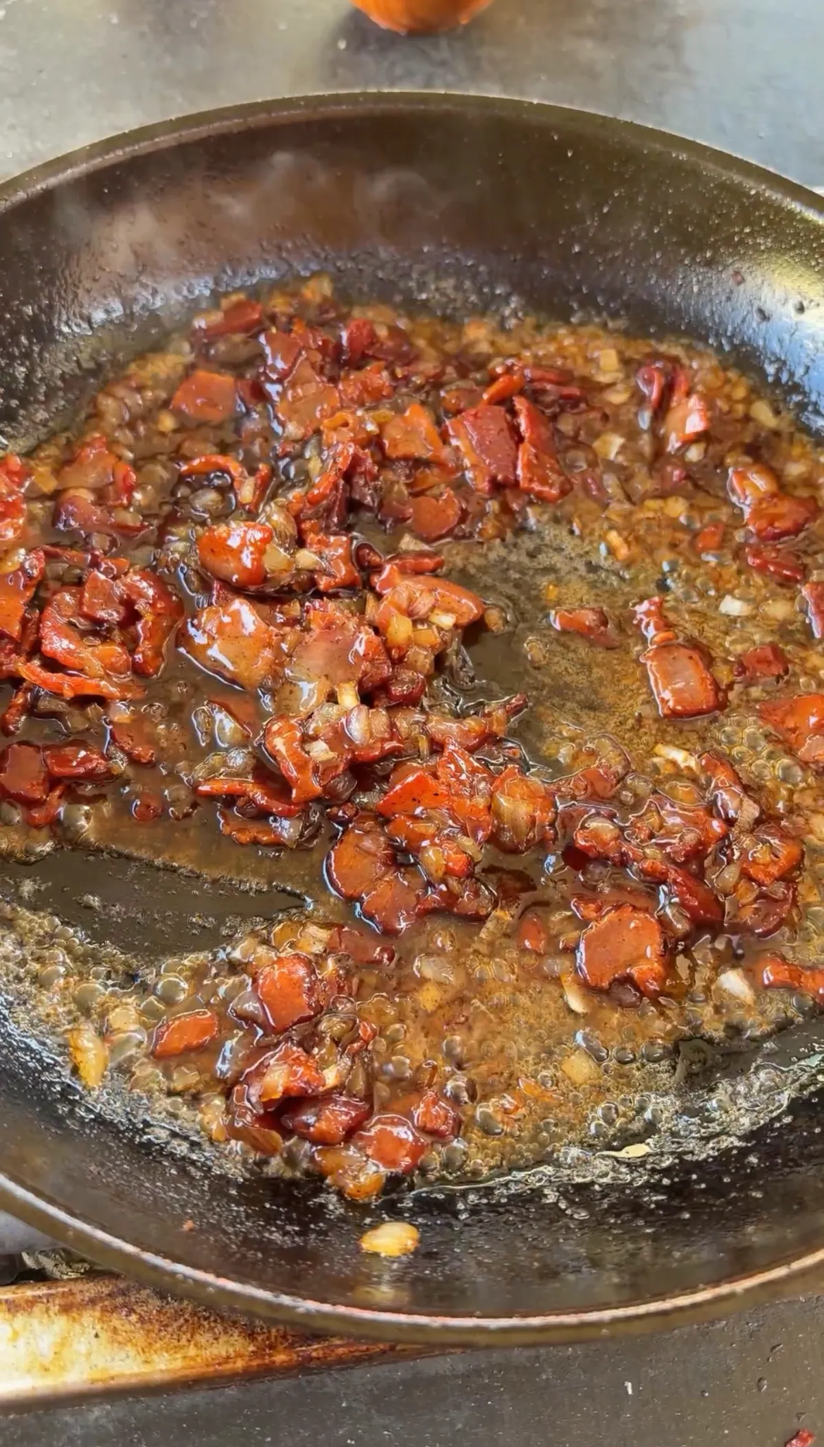 Chopped bacon simmering with diced onion, brown sugar, and maple syrup in a skillet to make bacon jam