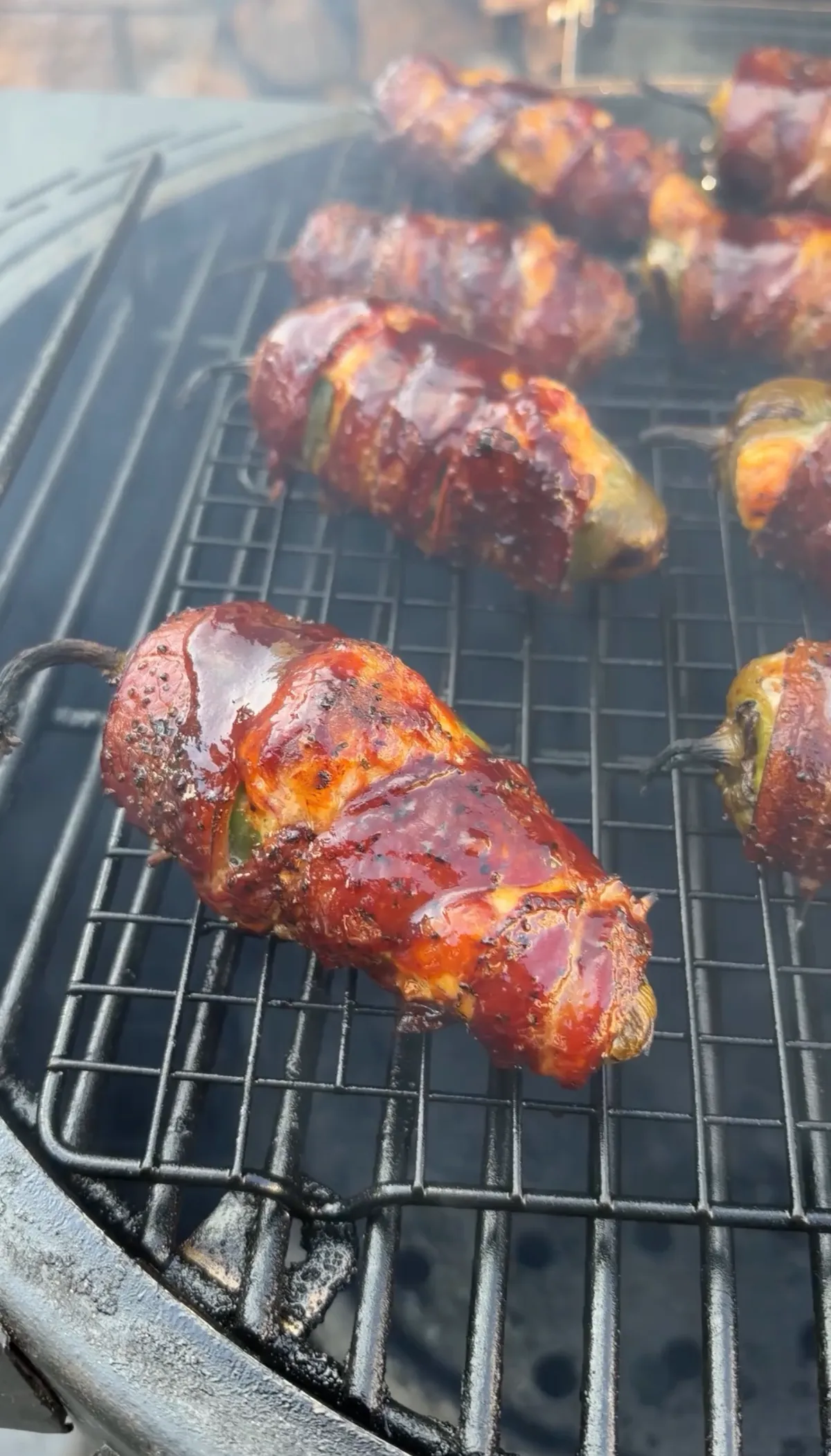 Bacon-wrapped brisket-stuffed jalapeño boats glazed with sticky BBQ sauce smoking on a grill grate