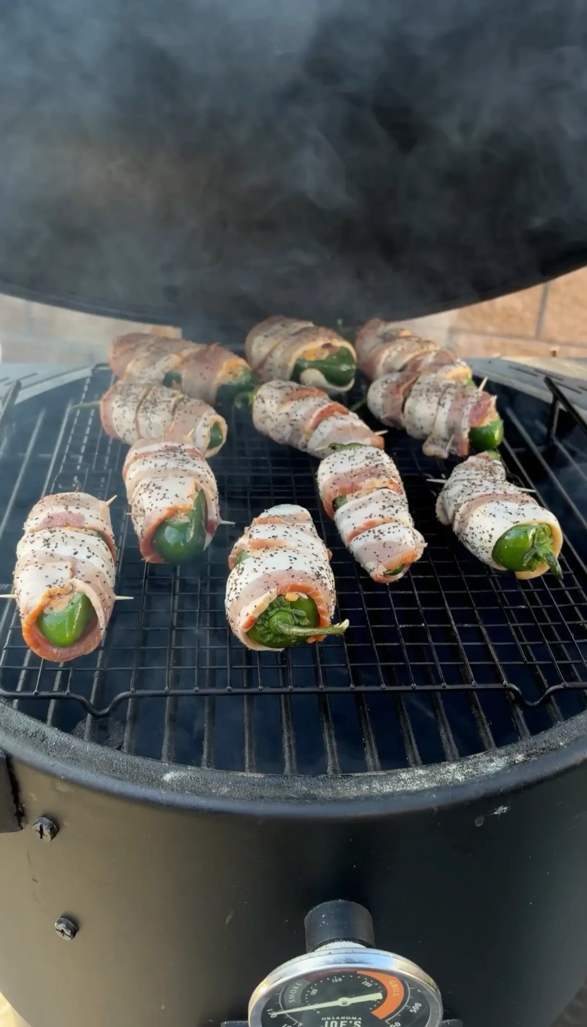 Bacon-wrapped brisket-stuffed jalapeño boats with black pepper on smoker grates at 250°F with applewood smoke