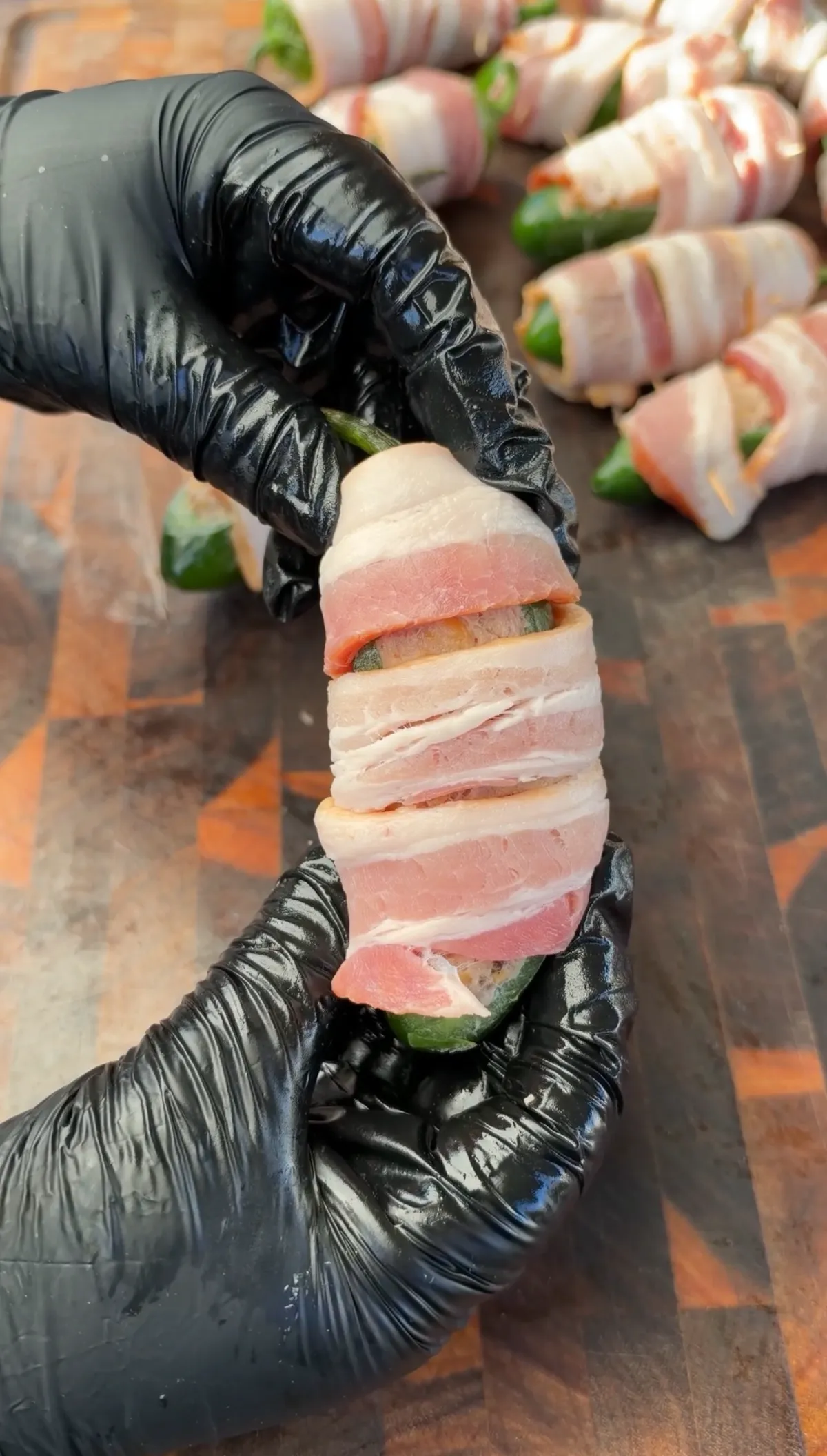 Gloved hands holding a thick-cut bacon-wrapped stuffed jalapeño boat secured with toothpicks, ready to smoke