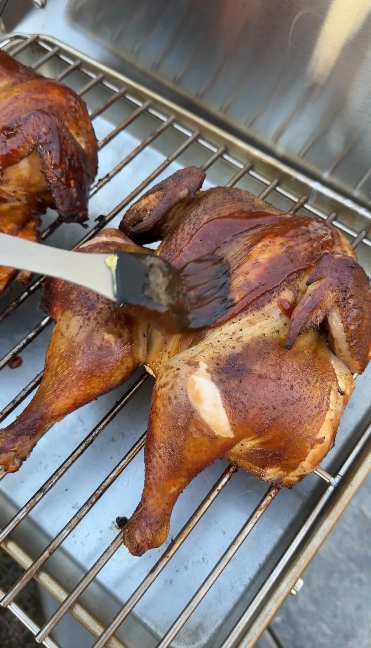 BBQ sauce being brushed onto applewood smoked spatchcock chicken on a smoker rack at 150°F glaze stage