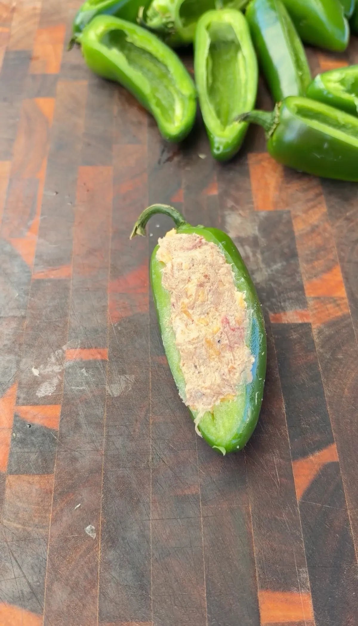 Halved jalapeño boat filled with smoked brisket, cream cheese, and cheddar mixture on a butcher block cutting board