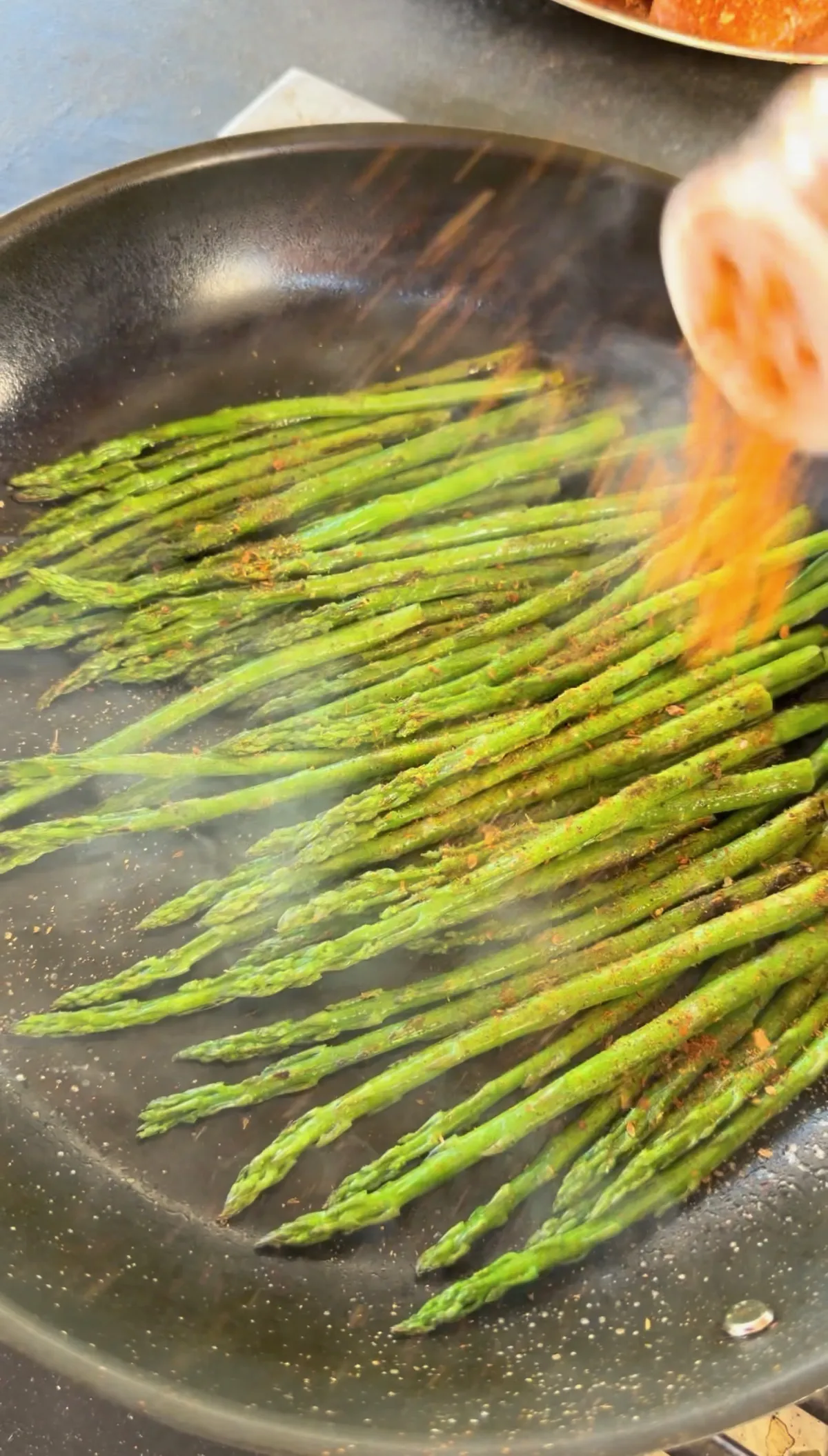Asparagus seasoned with Cajun seasoning charring in a hot skillet, being sprinkled with spice