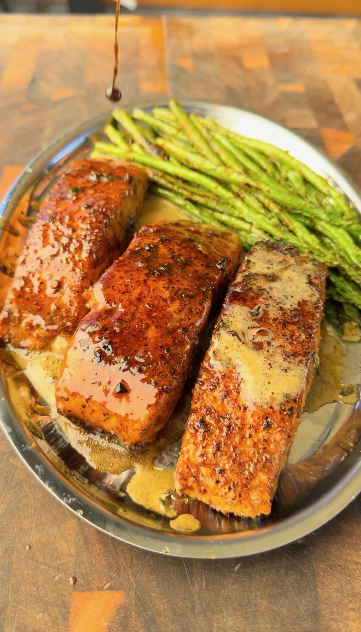 Butter-basted Cajun pan-seared salmon portions with charred asparagus on a steel plate, drizzled with thyme-infused butter