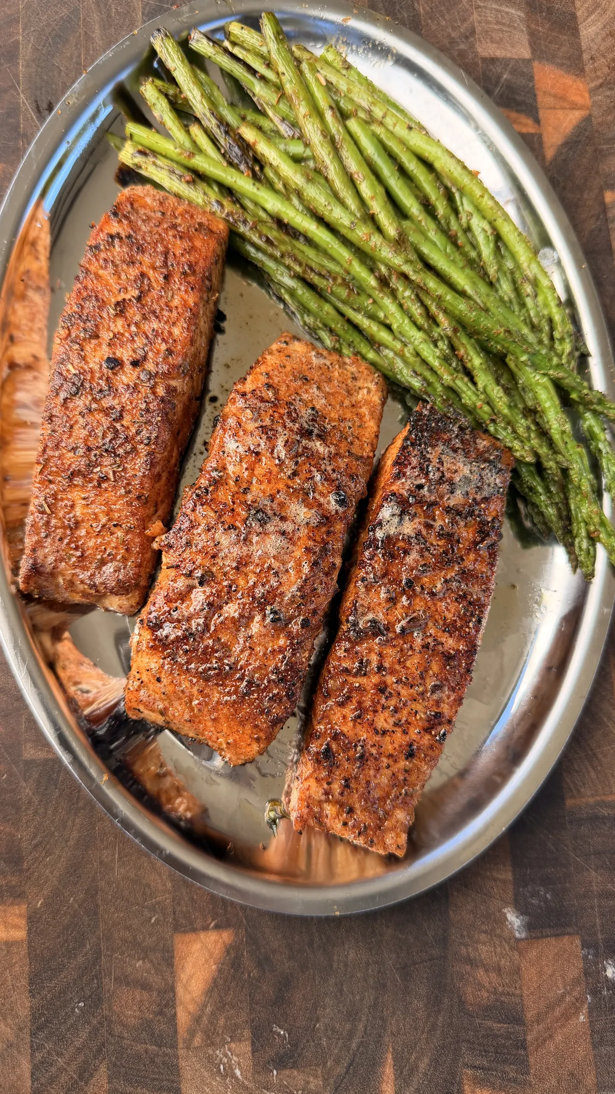 Three Cajun-seasoned pan-seared salmon portions served with charred asparagus on a stainless steel platter