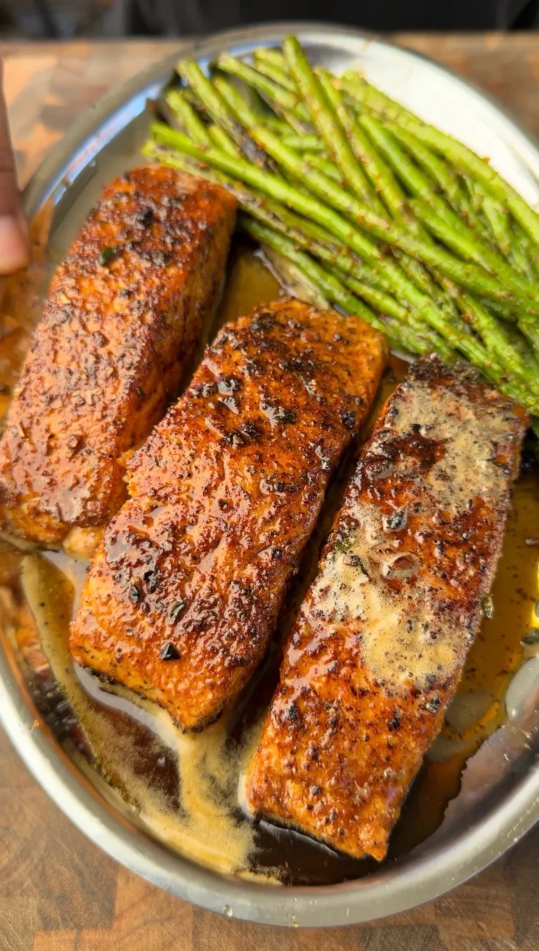 Three butter-basted Cajun-seasoned pan-seared salmon portions with thyme-infused butter and charred asparagus on a skillet