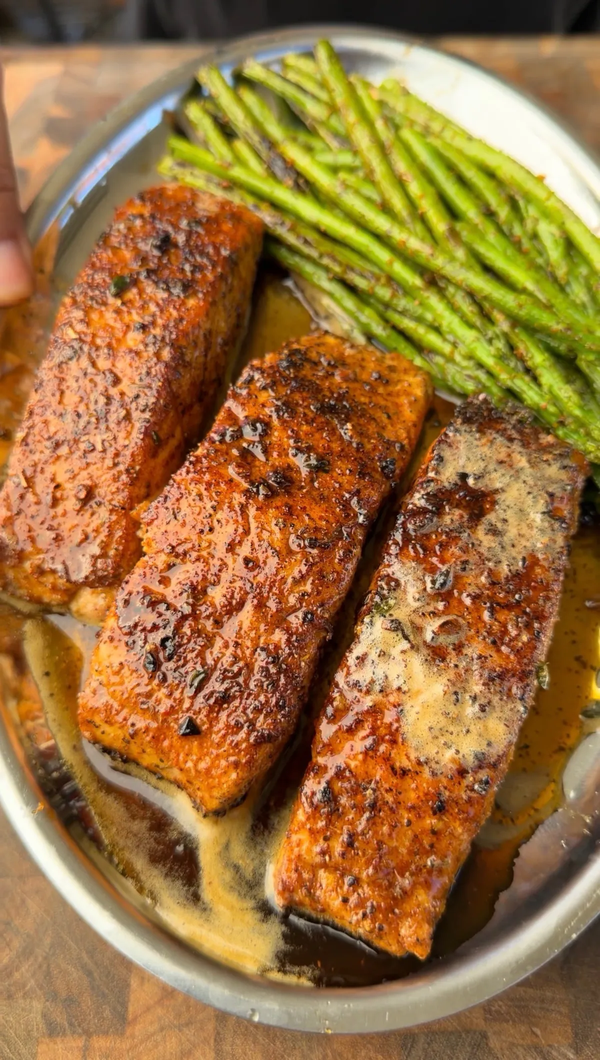 Three butter-basted Cajun-seasoned pan-seared salmon portions with thyme-infused butter and charred asparagus on a skillet