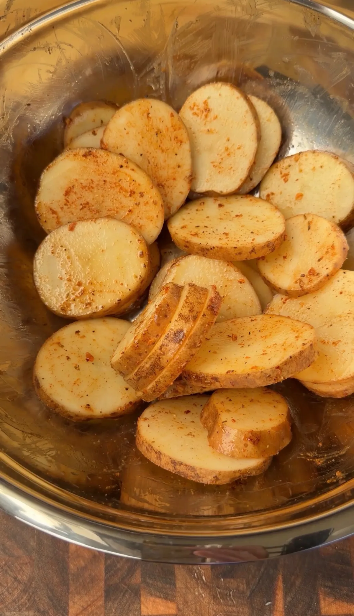 Russet potato slices tossed in olive oil and Cajun seasoning in a stainless steel mixing bowl